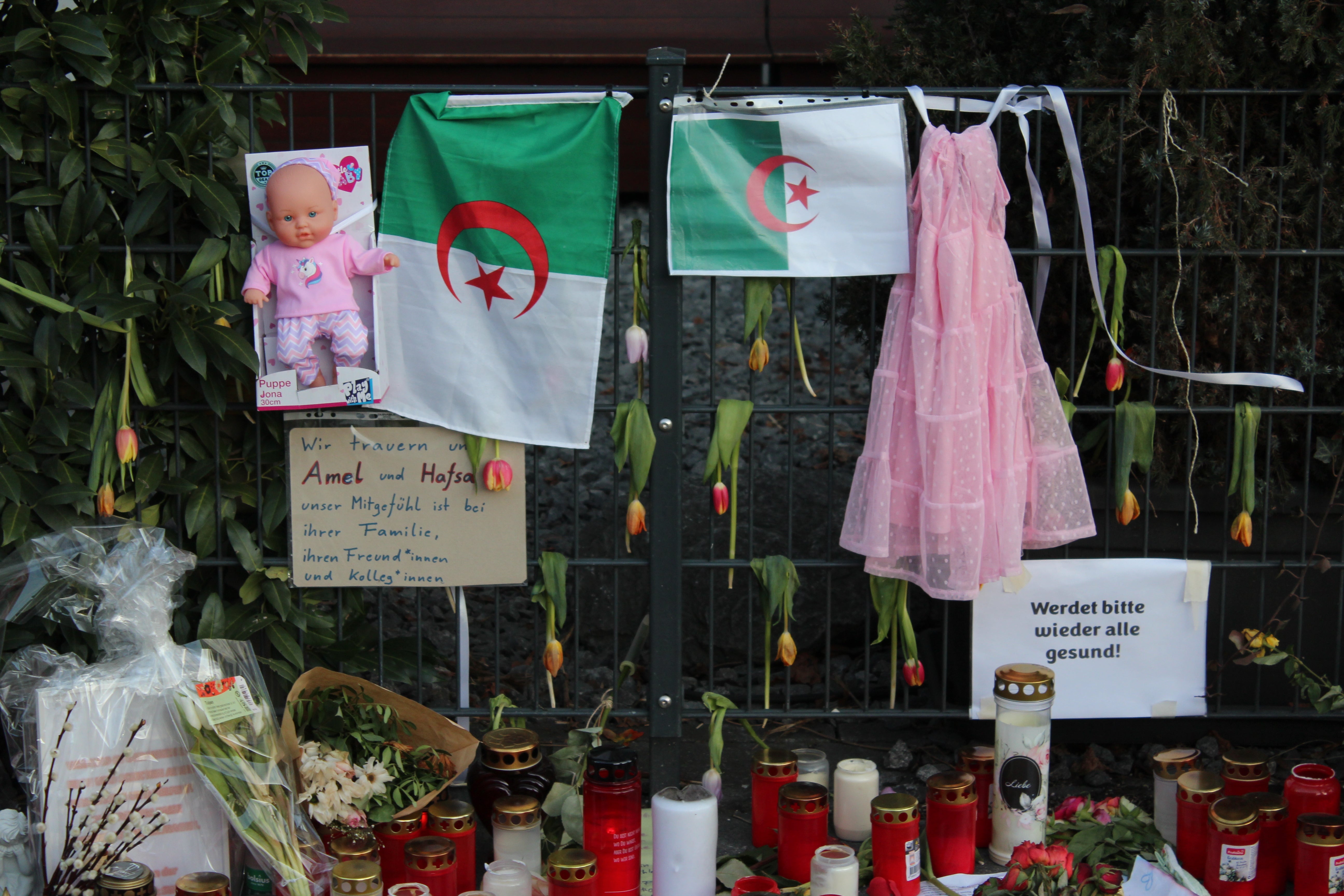 A pink dress and a baby doll are hung on either side of Algerian flags at a tribute in Munich at the scene of the attack