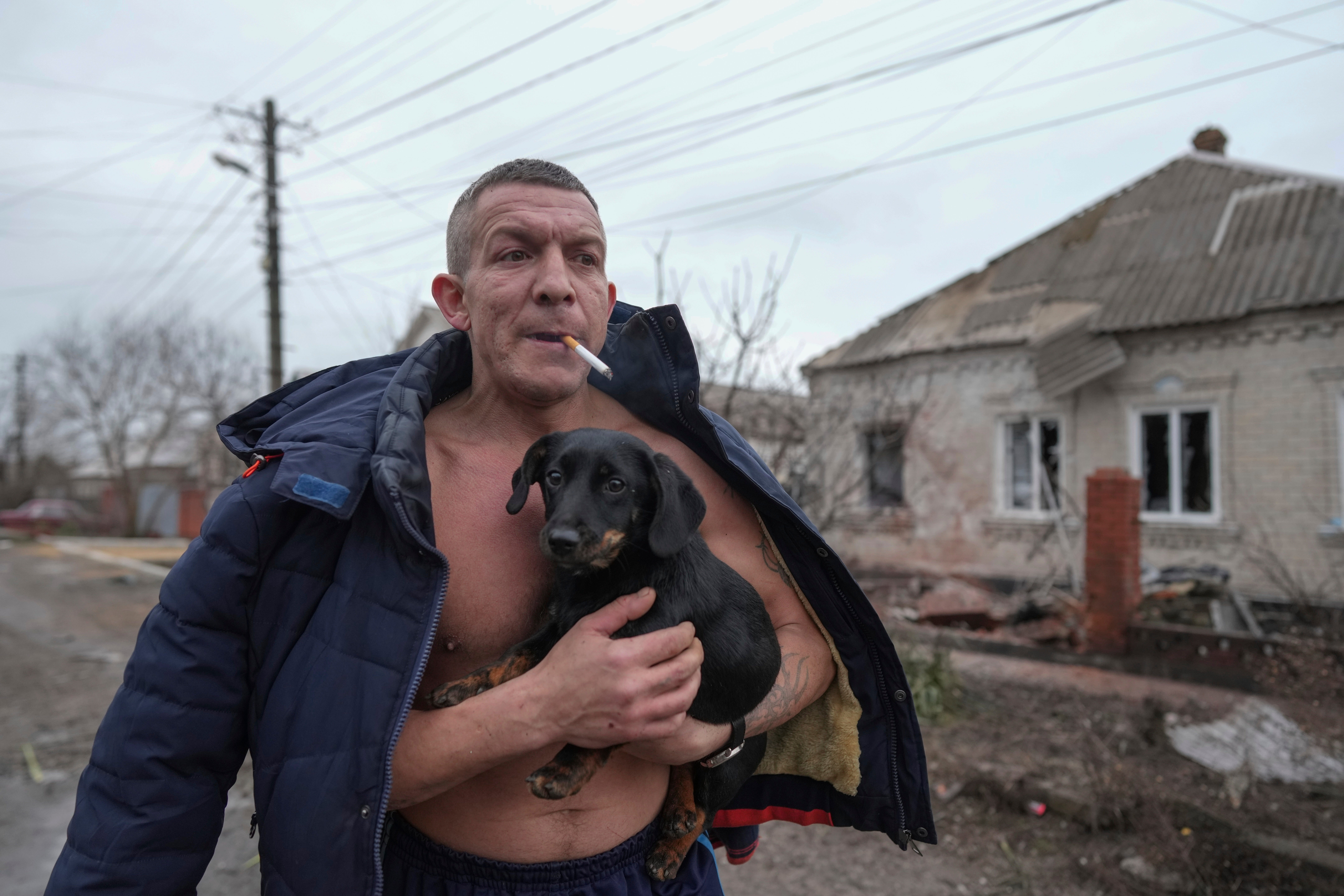 A man holds a dog as he walks past a damaged house following Russian shelling, in Mariupol, Ukraine, Thursday, Feb. 24, 2022