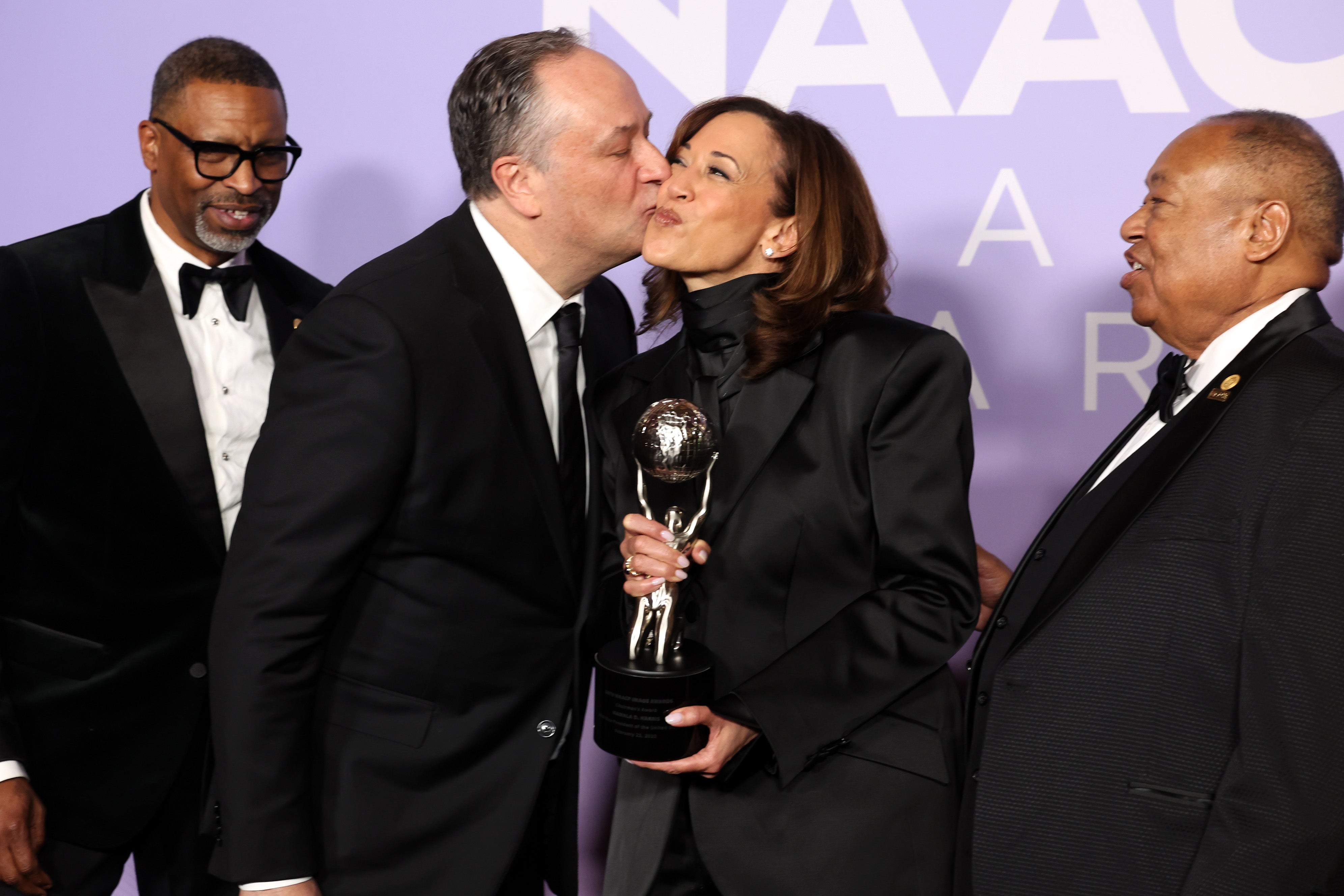 Kamala Harris holds the NAACP Image Award — Chairman's Award while her husband, Doug Emhoff, kisses her cheek