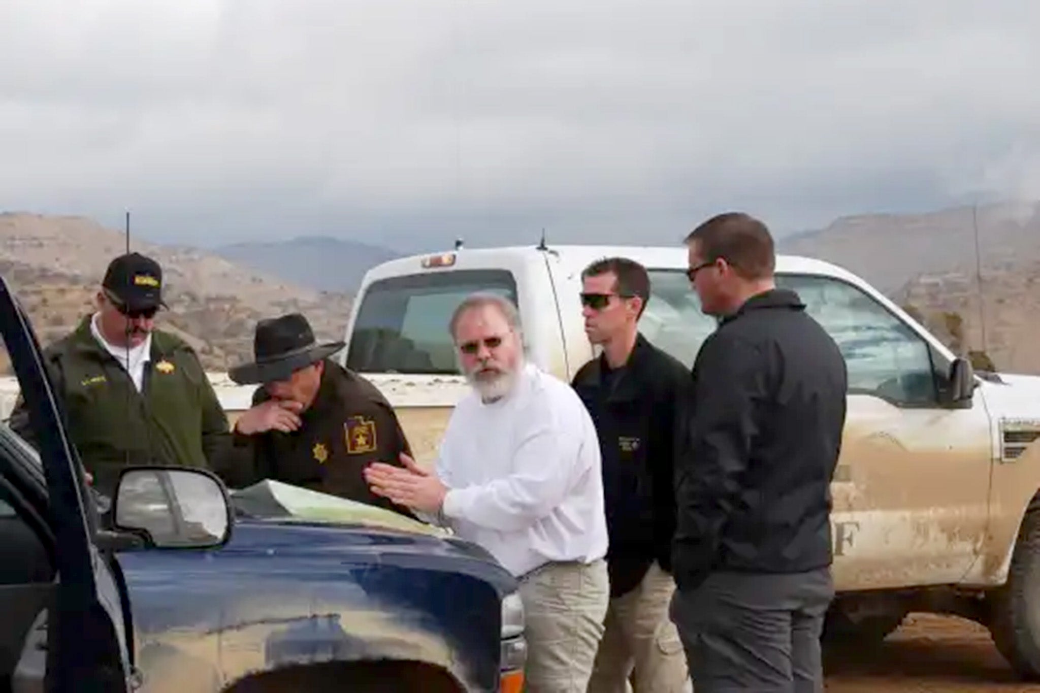 Jonny Grusing is pictured standing behind Scott Kimball (white shirt) during a search for his victims in a remote, mountainous area near Colorado and Utah