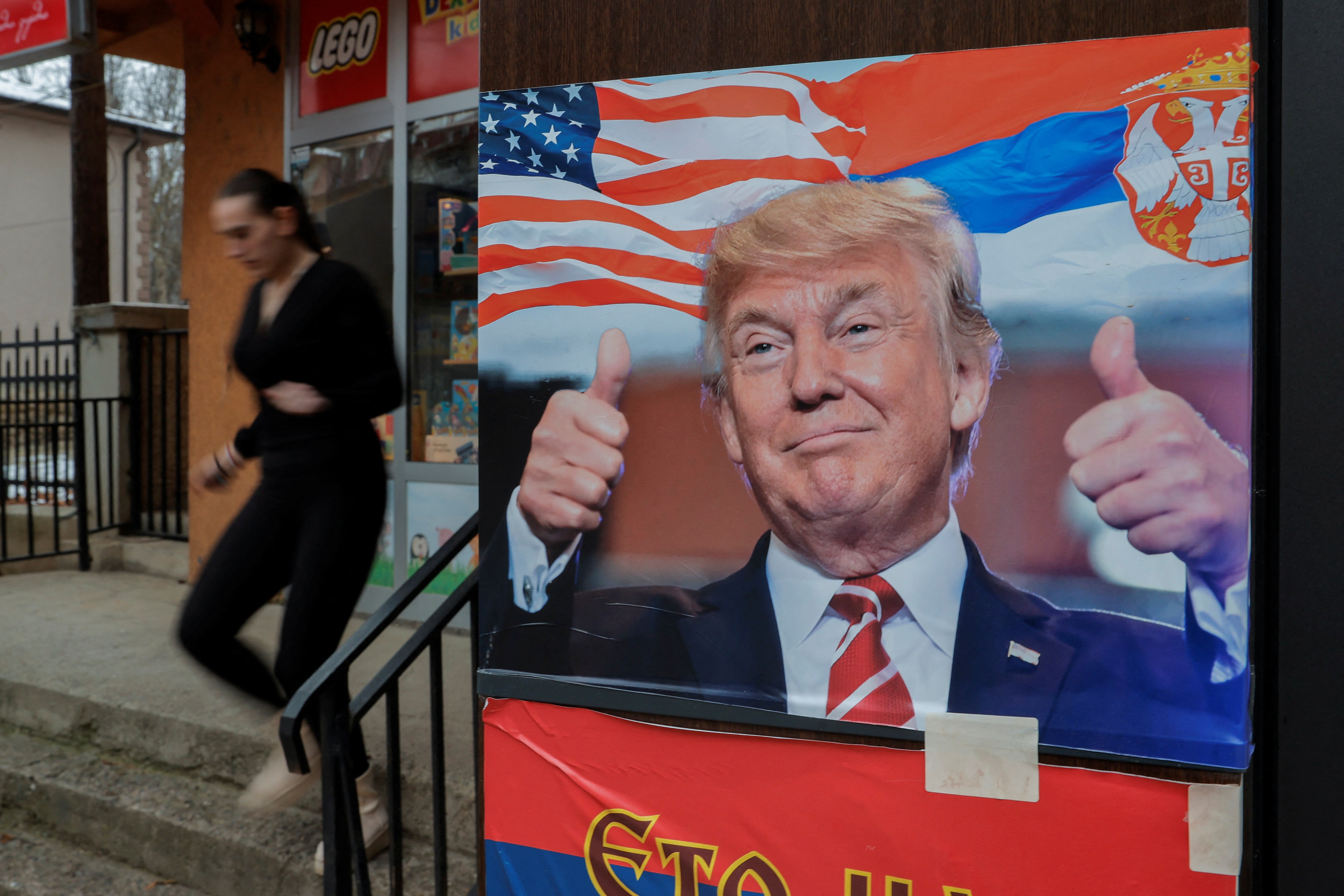 A woman walks near a poster showing Trump with a Serbian flag, in Mitrovica, Kosovo in January