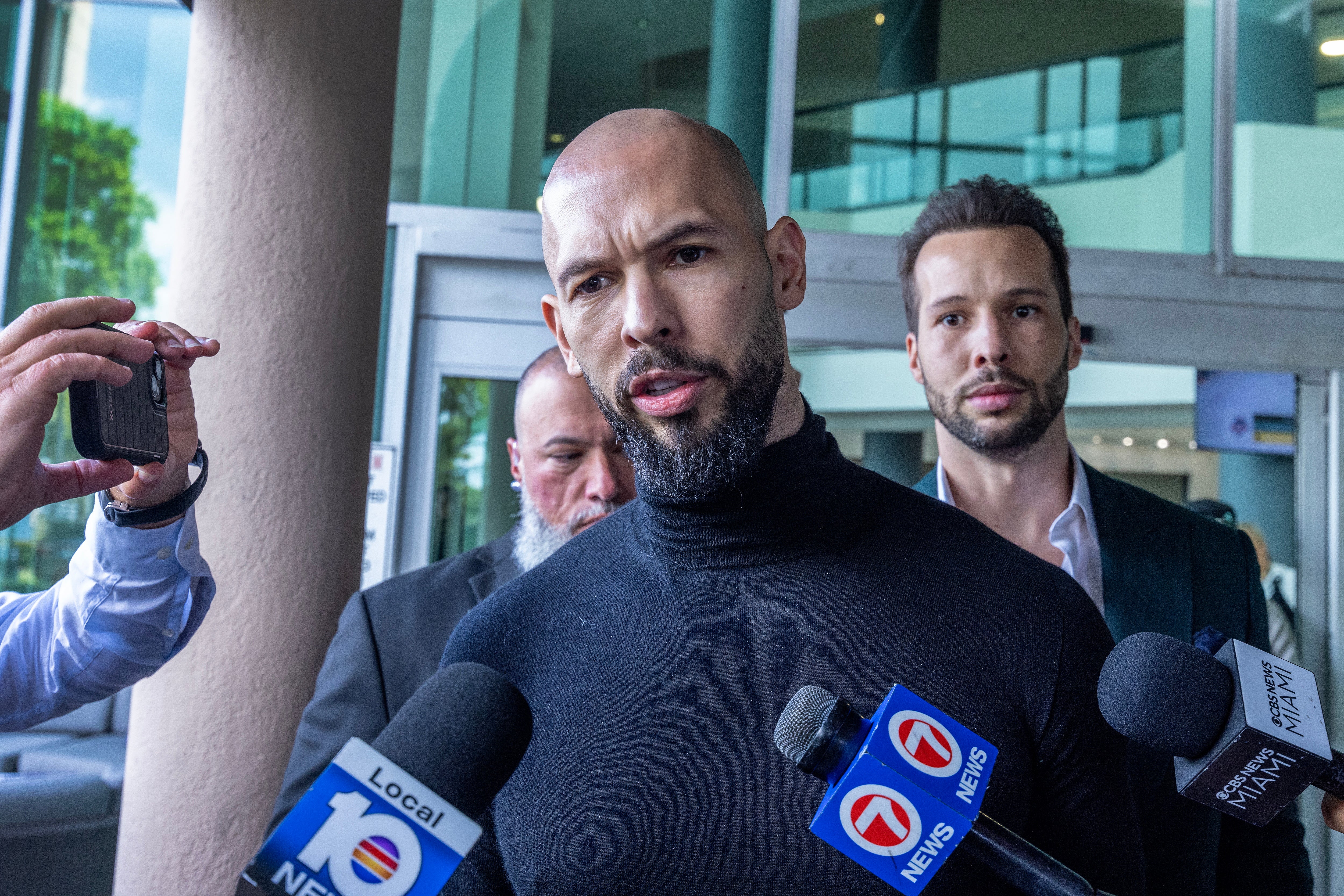 Andrew Tate and his brother Tristan, behind, speaking to reporters after landing in Florida