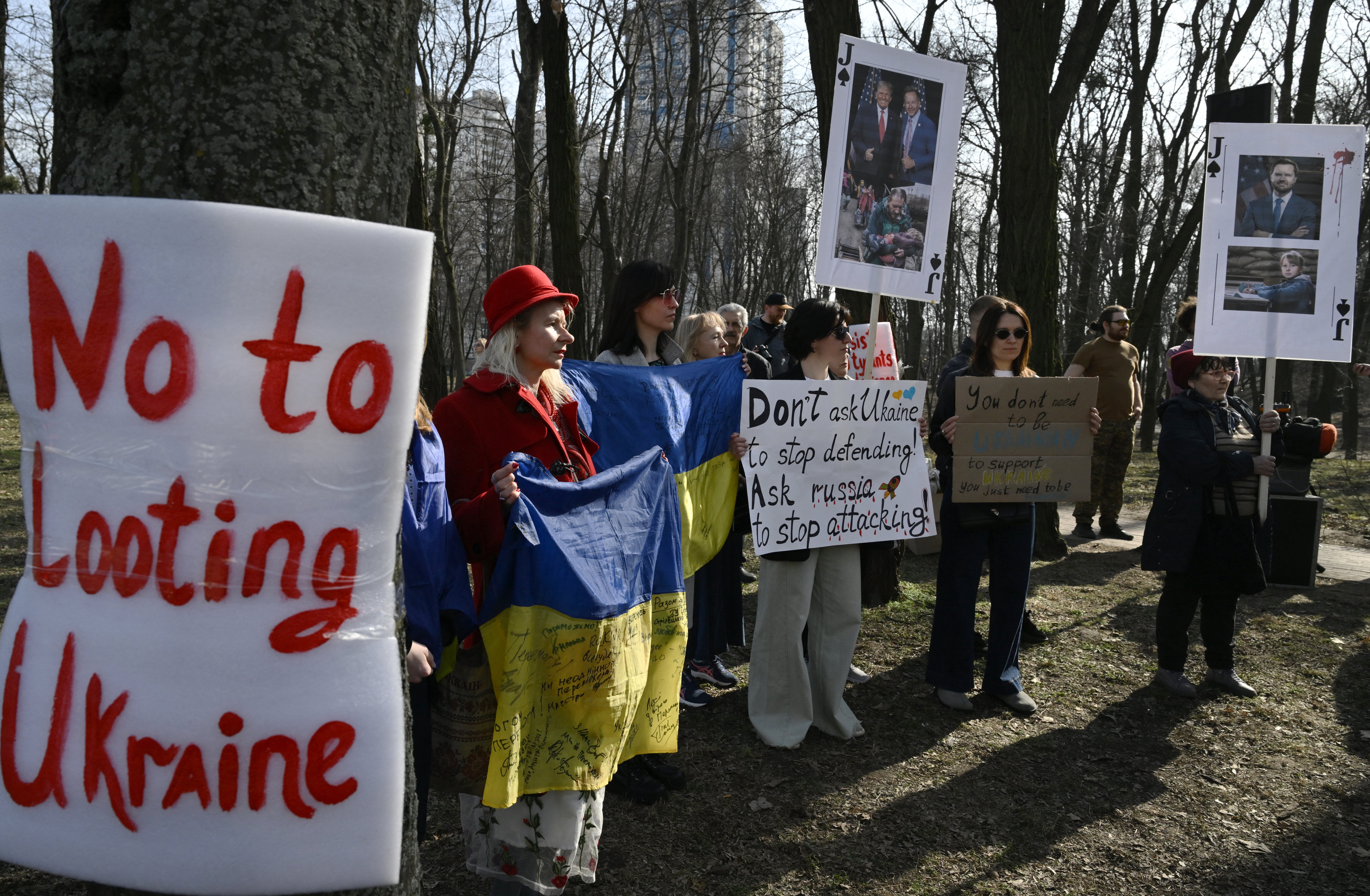 Demonstrators hold placards as they stand next to a sign reading ‘no to looting Ukraine’ during a protest called ‘America, wake up’ on Saturday