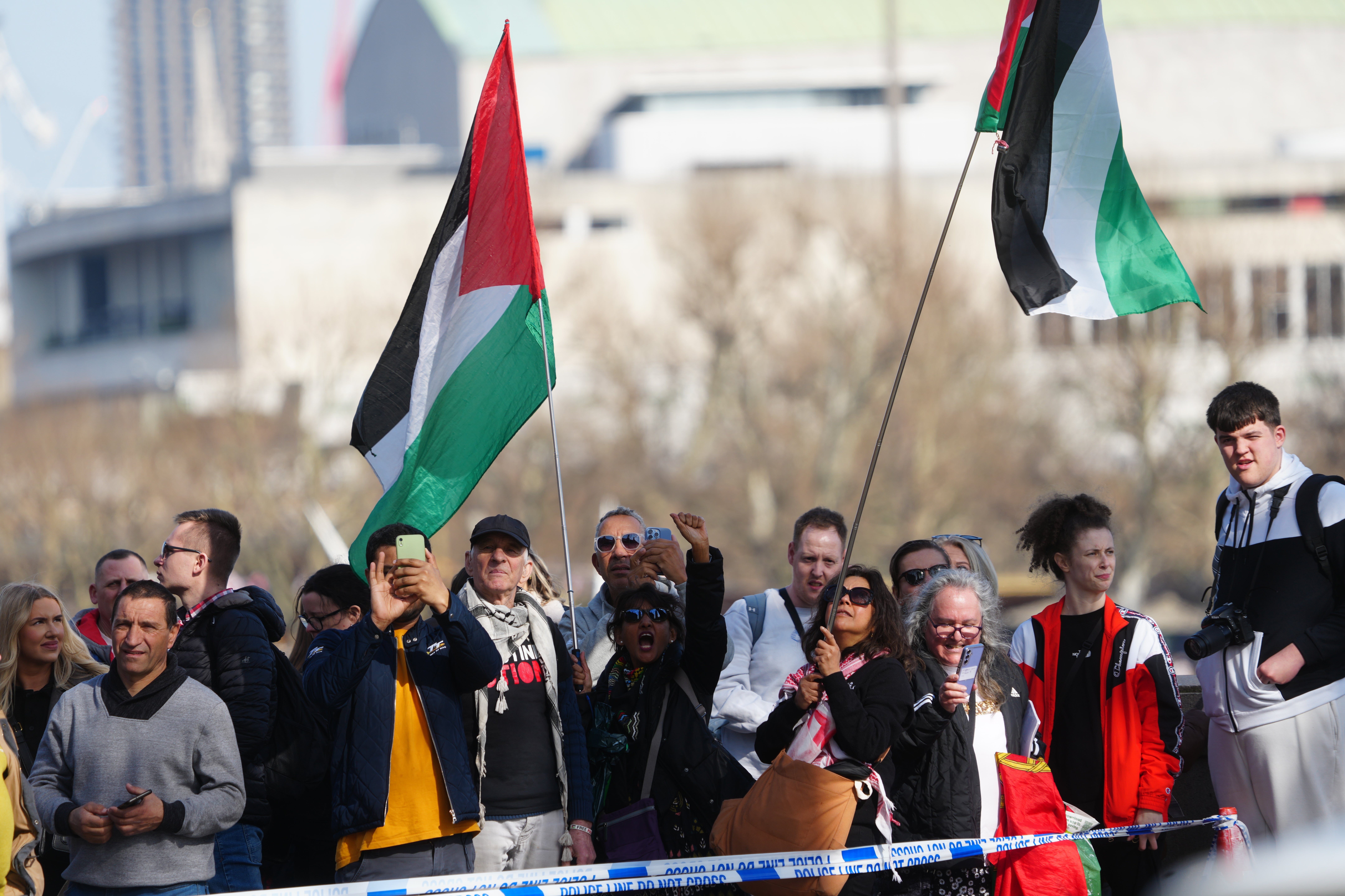 People holding Palestinian flags look on from behind a police cordon