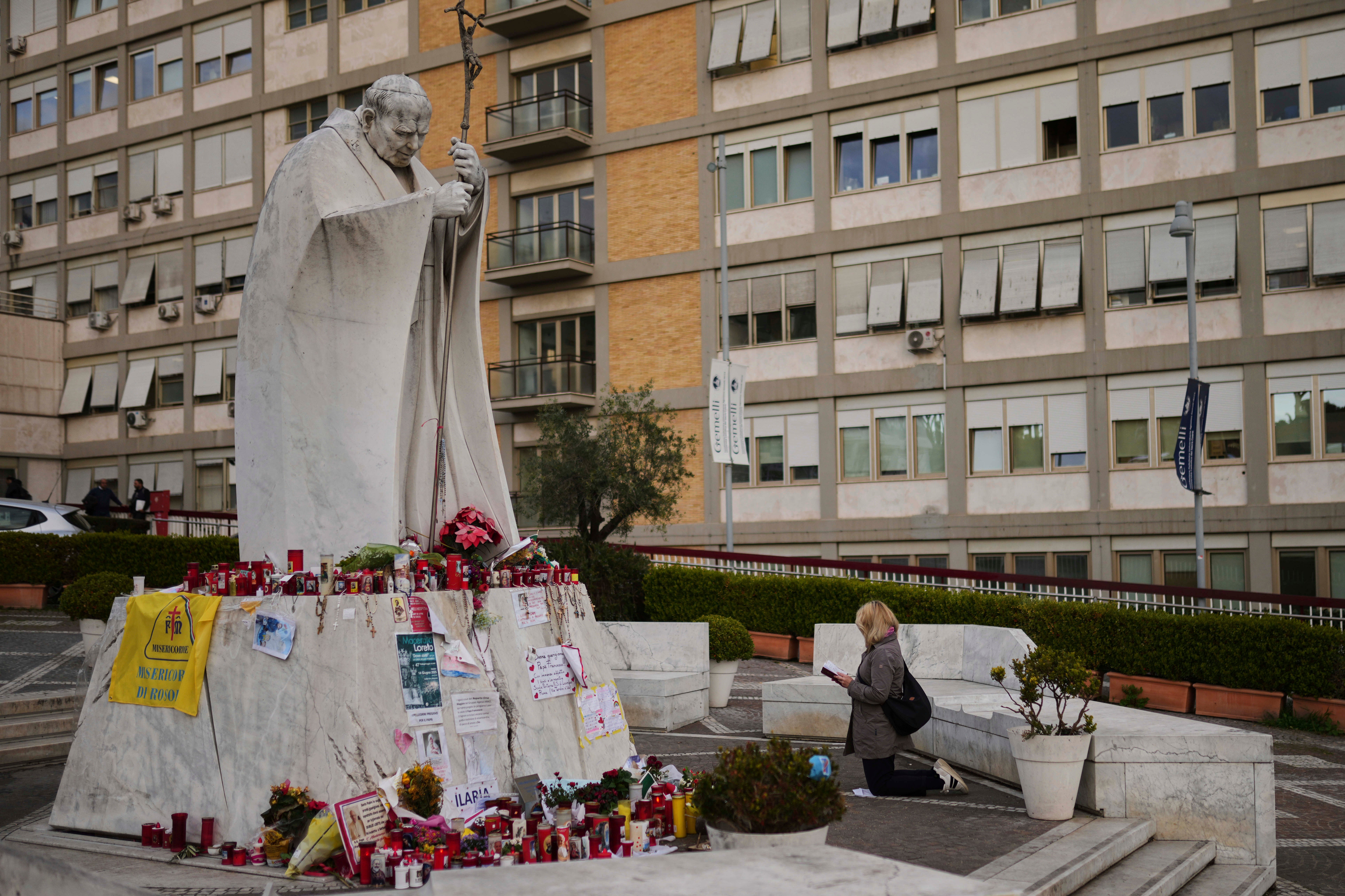 A woman prays next to the statue of Pope John Paul II outside the Gemelli hospital where Francis is being treated