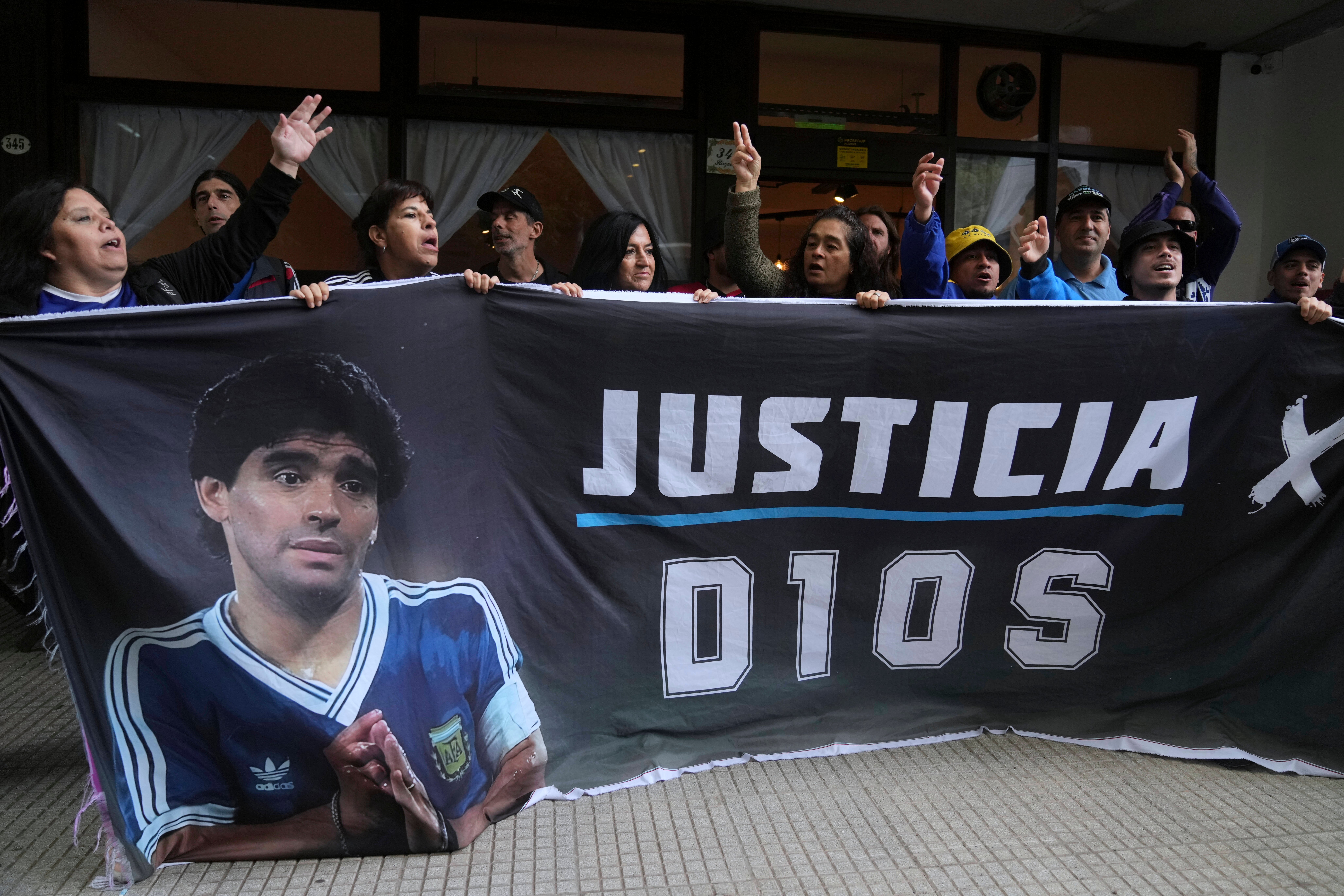 Fans of the late soccer star Diego Maradona hold a banner that reads in Spanish ‘Justice for God’ outside the court where members of the medical team that treated Maradona go on trial for alleged homicide by negligence in San Isidro on the outskirts of Buenos Aires, Argentina, Tuesday, March 11, 2025. (AP Photo/Natacha Pisarenko)