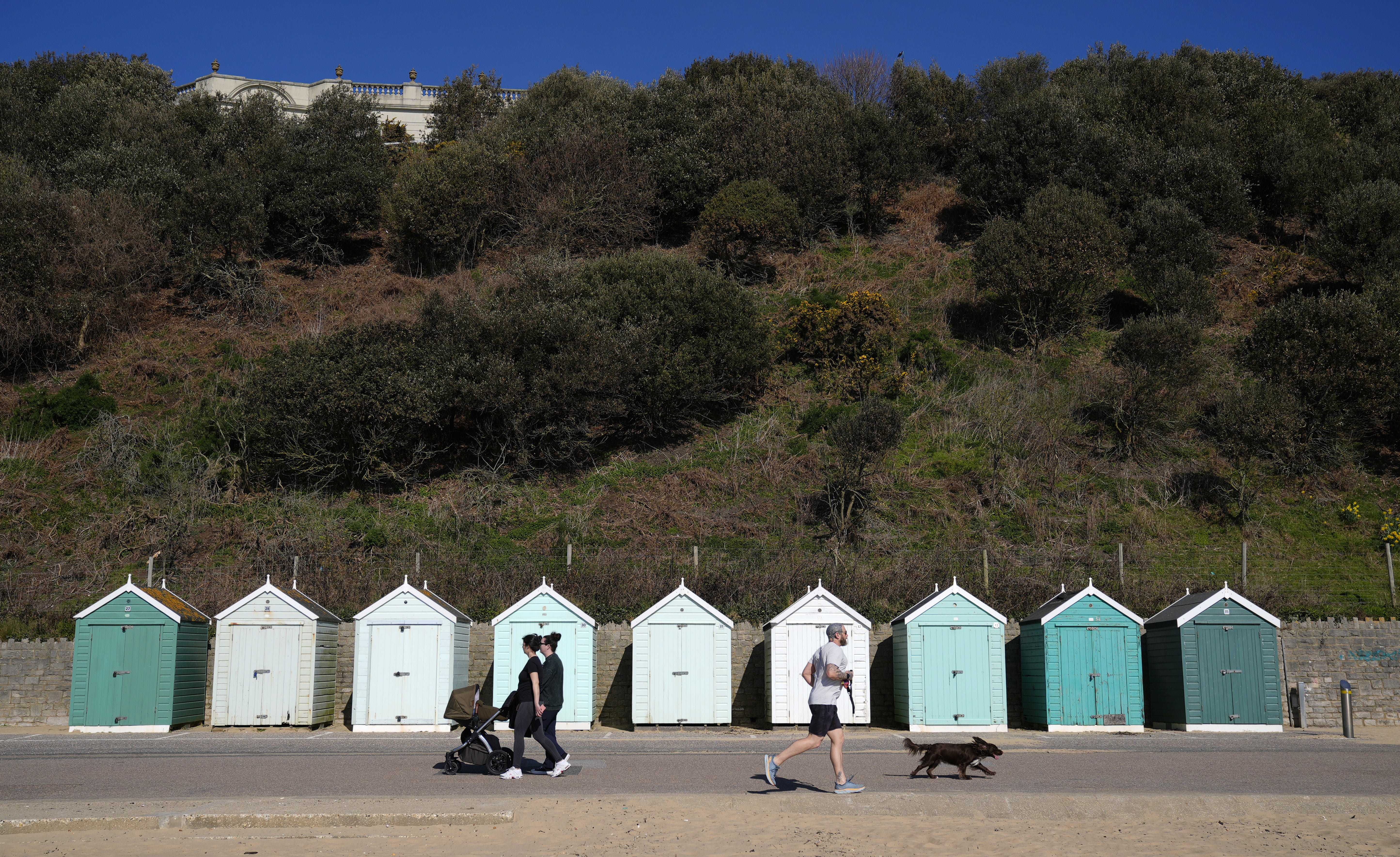 People walk past beach huts on Bournemouth Beach in Dorset