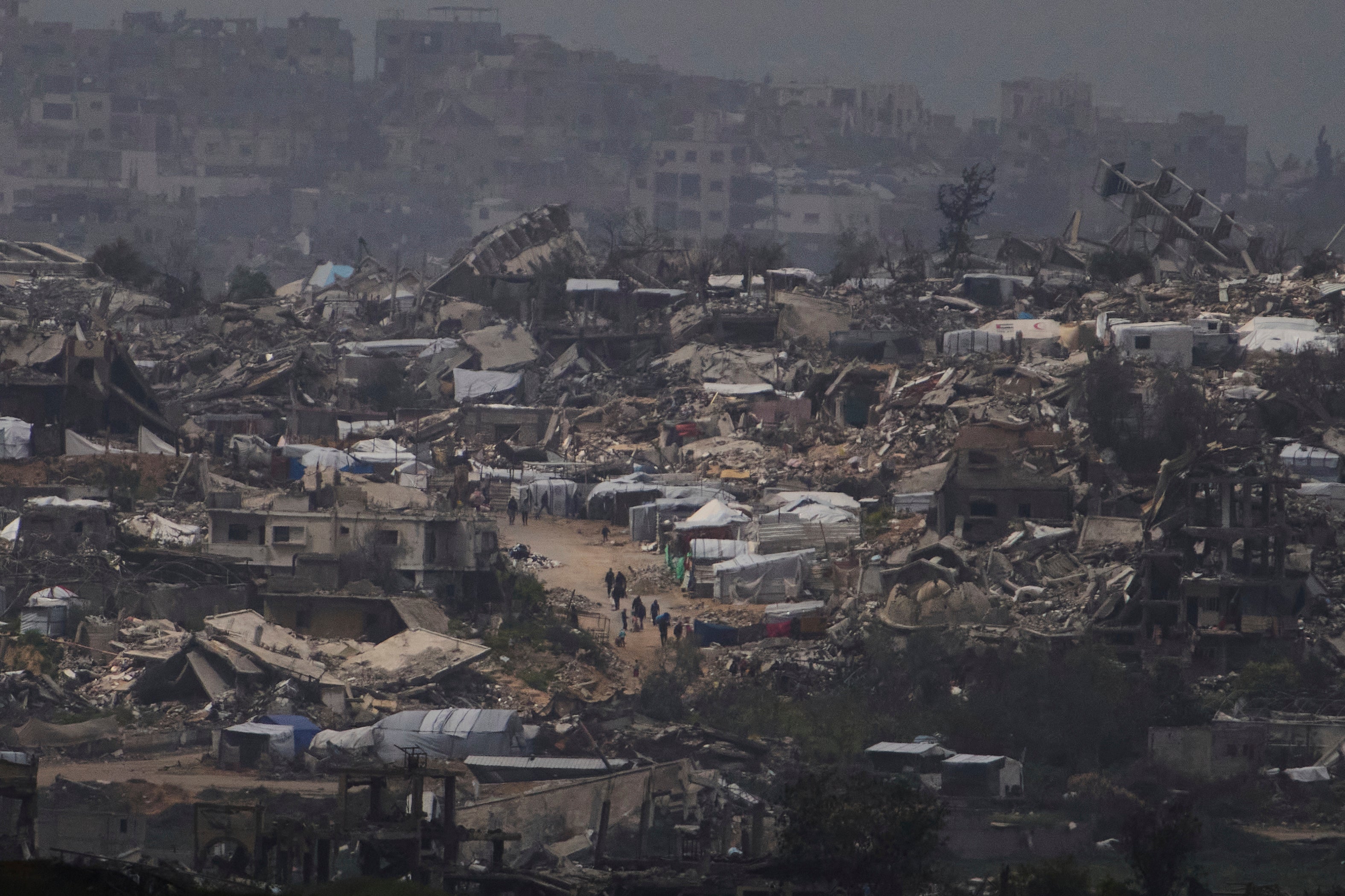 People walking surrounded by buildings destroyed during the Israeli air and ground offensive in the Gaza Strip are seen from southern Israel on March 20, 2025