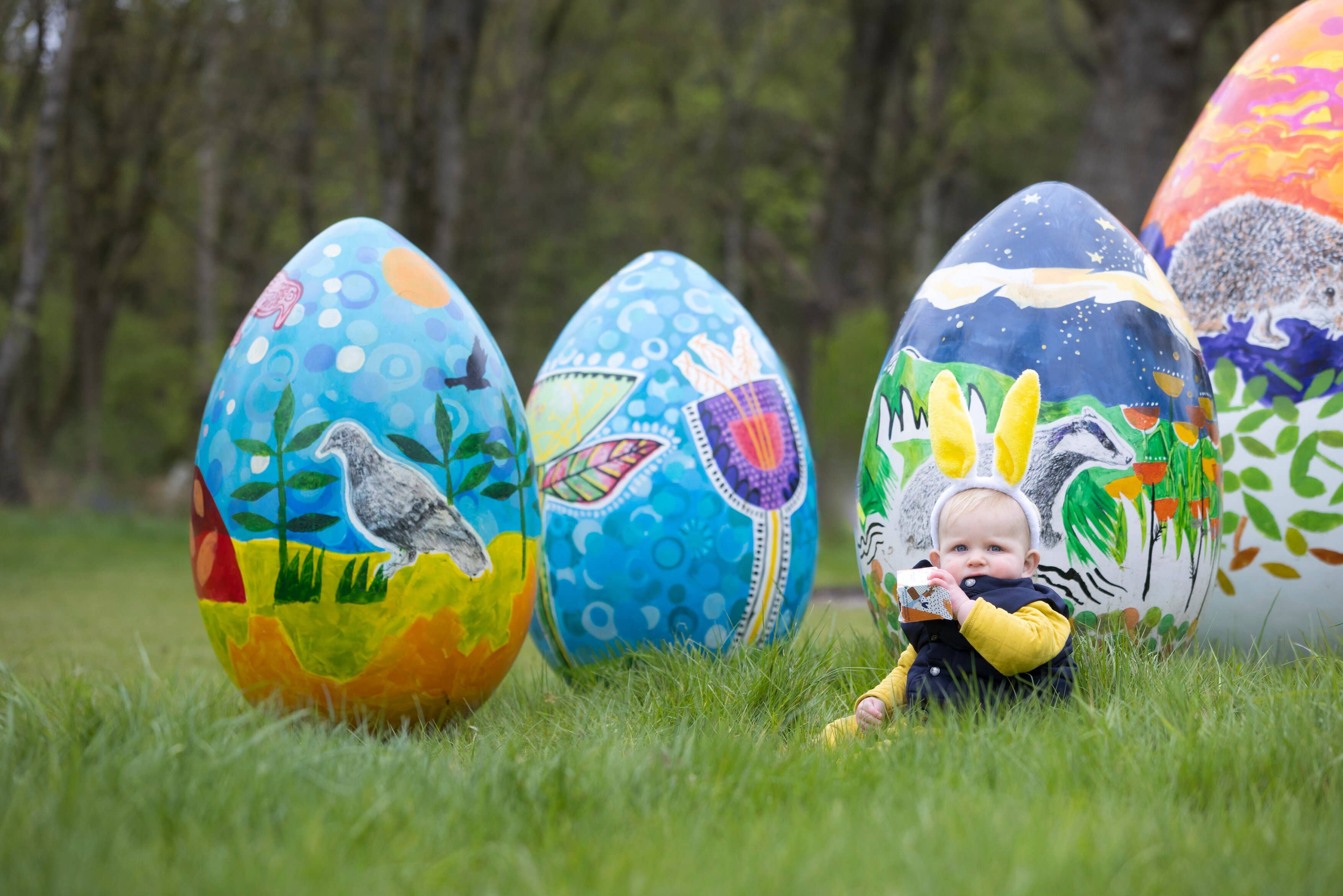 A child sitting next to giant painted Easter eggs at RHS Garden Bridgewater (RHS/PA)