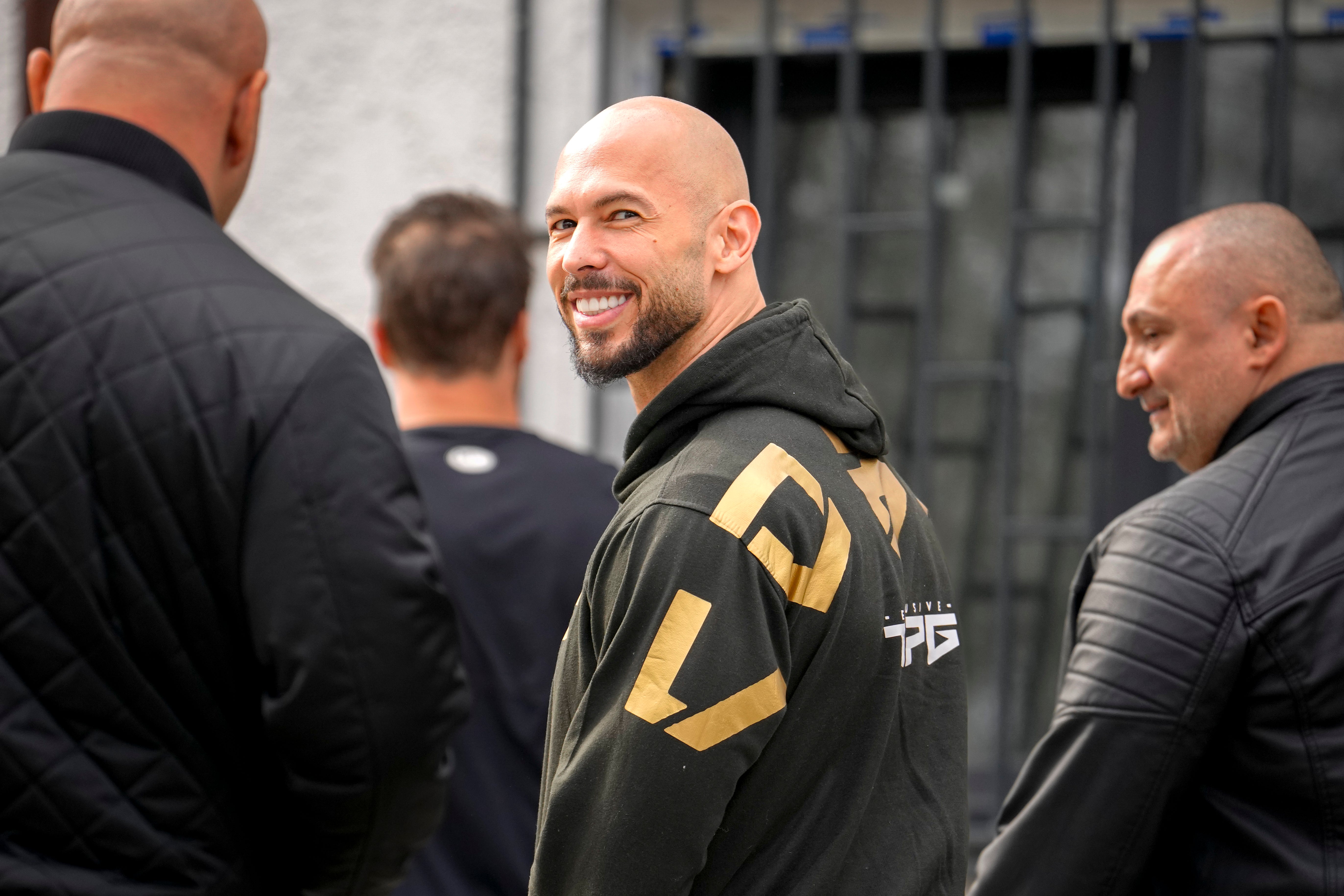 Andrew Tate, center, arrives at a police station to checking in as part of his judicial control, which requires him to appear before judicial authorities in Romania when summoned, after returning from the United States, in Voluntari, Romania, Monday, March 24, 2025. (AP Photo/Vadim Ghirda)