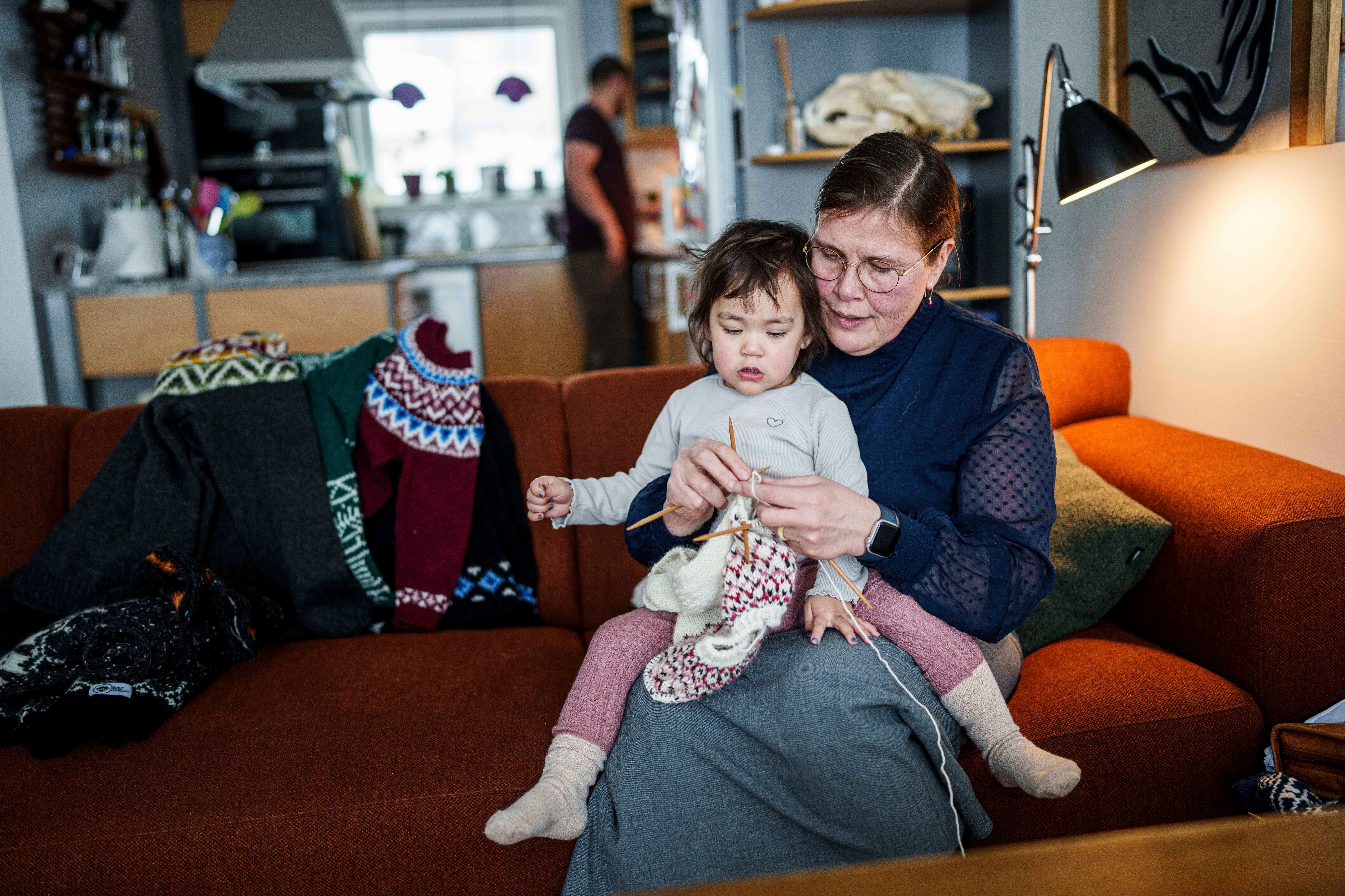 Lisa Sólrun Christiansen knits a sweater at her home in Nuuk while holding her granddaughter Siilia