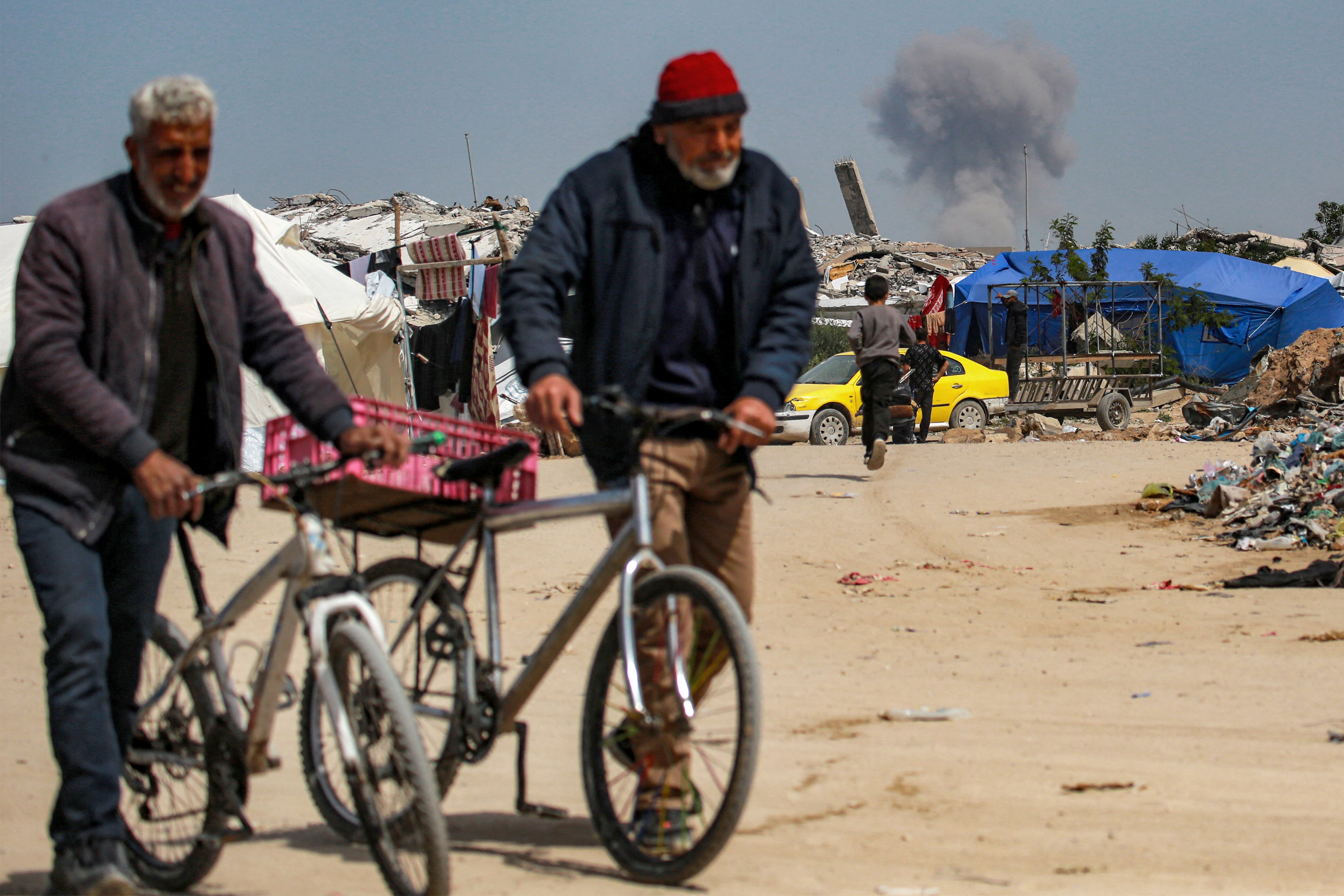 Two elderly men walk while a cloud of smoke erupts in the northern Gaza Strip