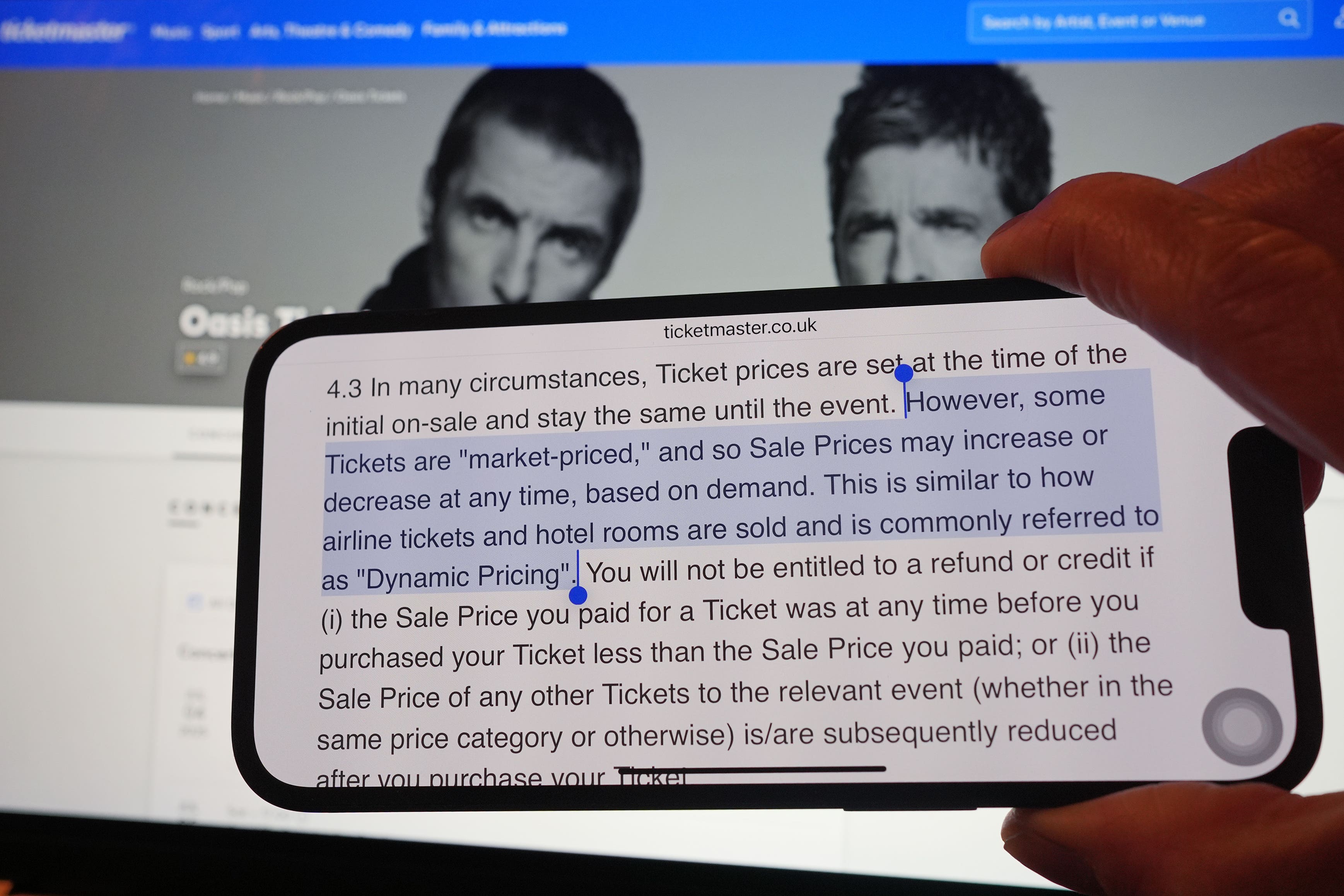 A section of Ticketmaster’s purchase policy explaining Dynamic Pricing, found on the company’s website, is highlighted on a phone, with the Tickemaster website displayed in the background, showing the options for purchasing Oasis tickets, in London (PA)