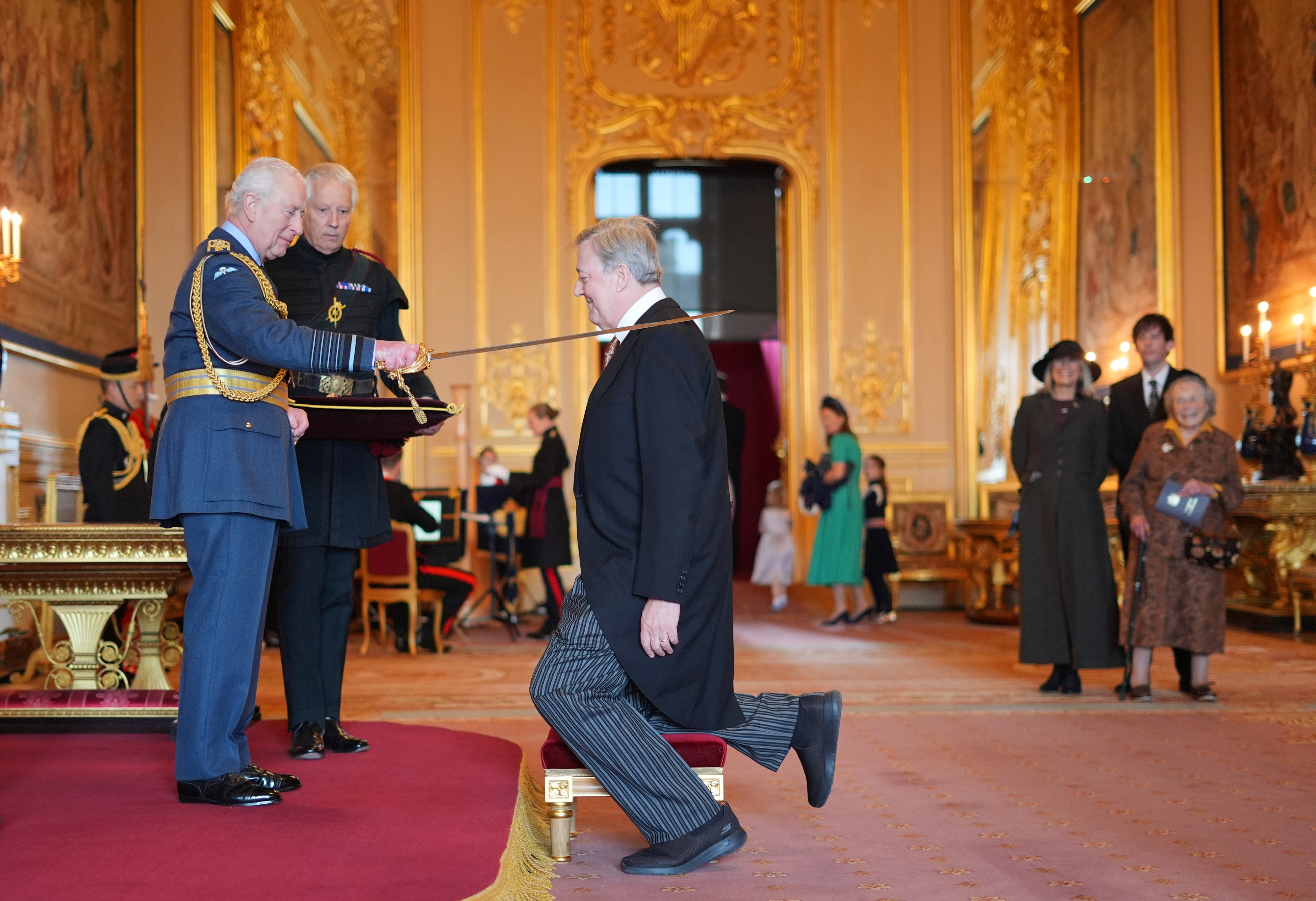 Sir Stephen Fry is made a Knight Bachelor by the King at Windsor Castle, watched by his family (Jordan Pettitt/PA)