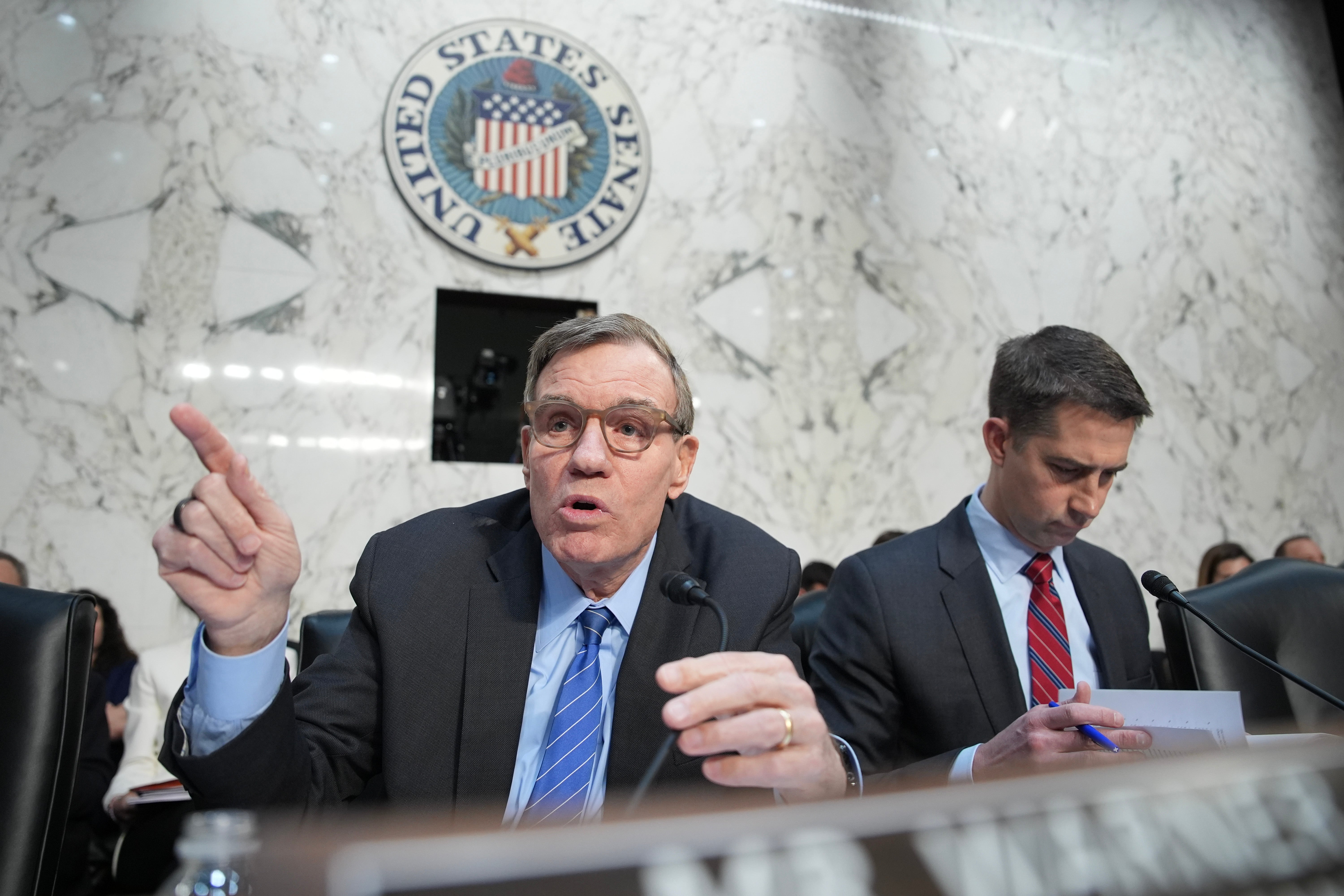 Democratic Senator Mark Warner, seated next to Republican Senator Tom Cotton, addresses top Trump administration officials during a Senate Intelligence Committee hearing