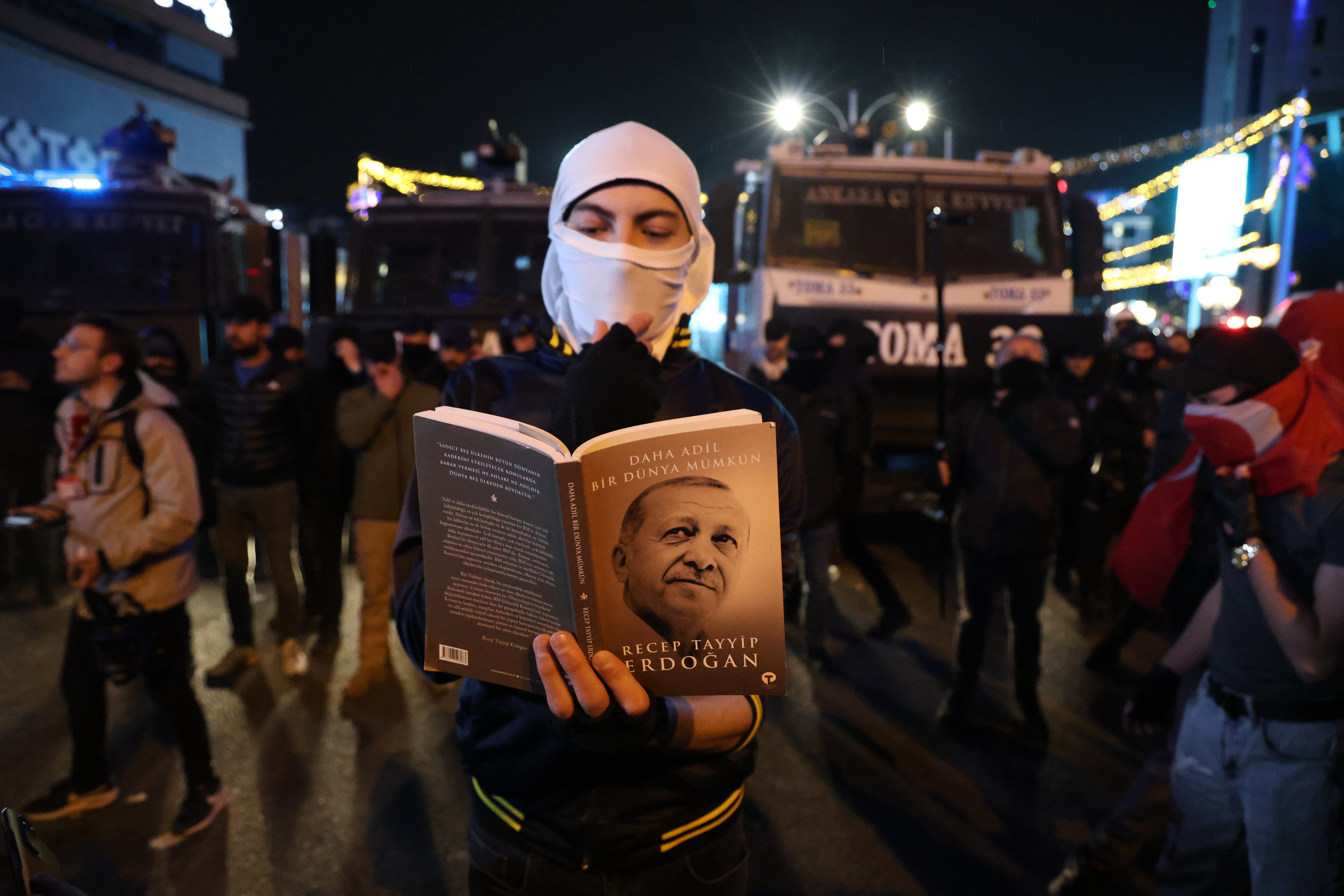 A protester reads President Erdogan's book in front of Turkish riot police barricades