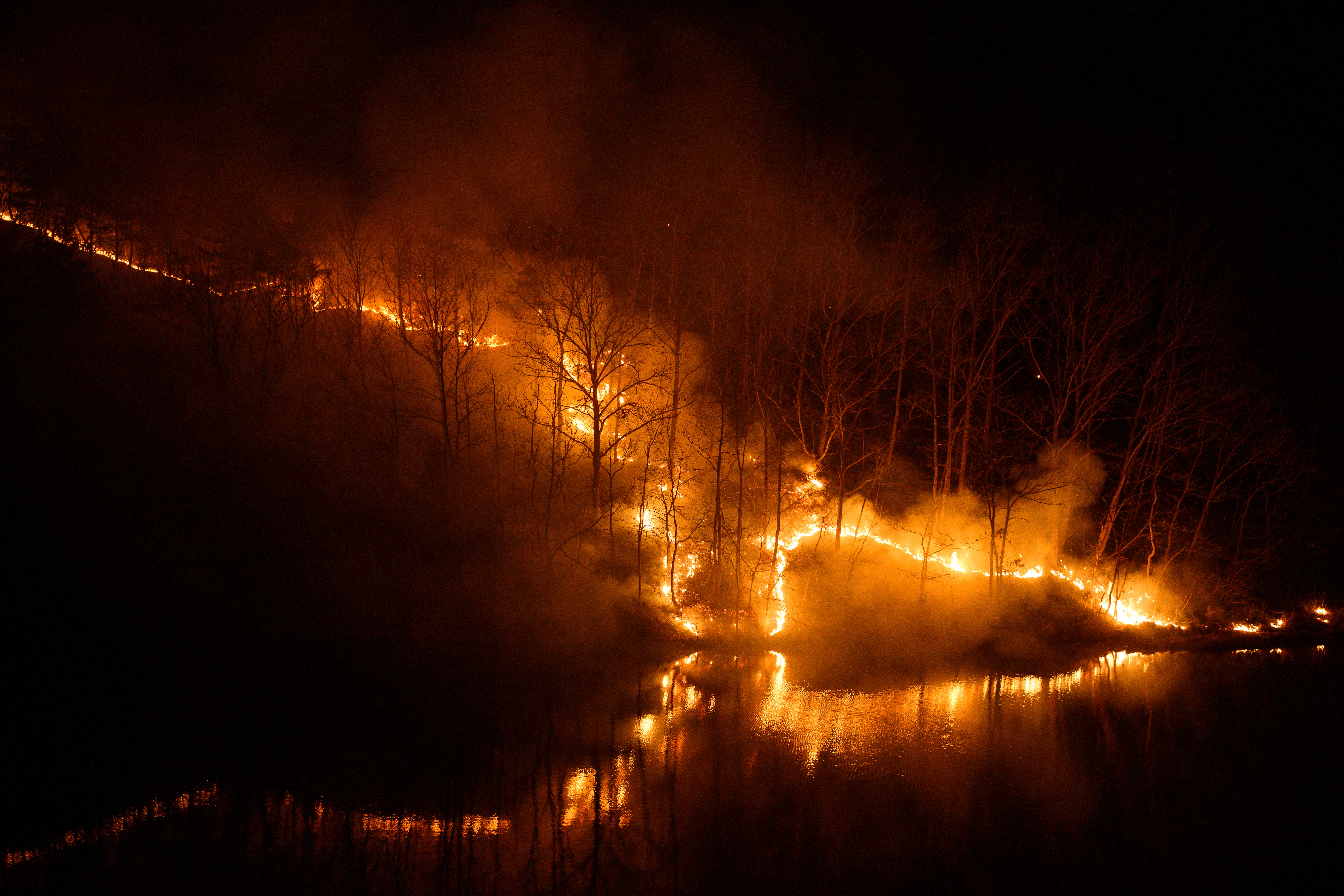 Smoke rises from burning trees as a wildfire is reflected in the waters of the Nakdong River in Andong