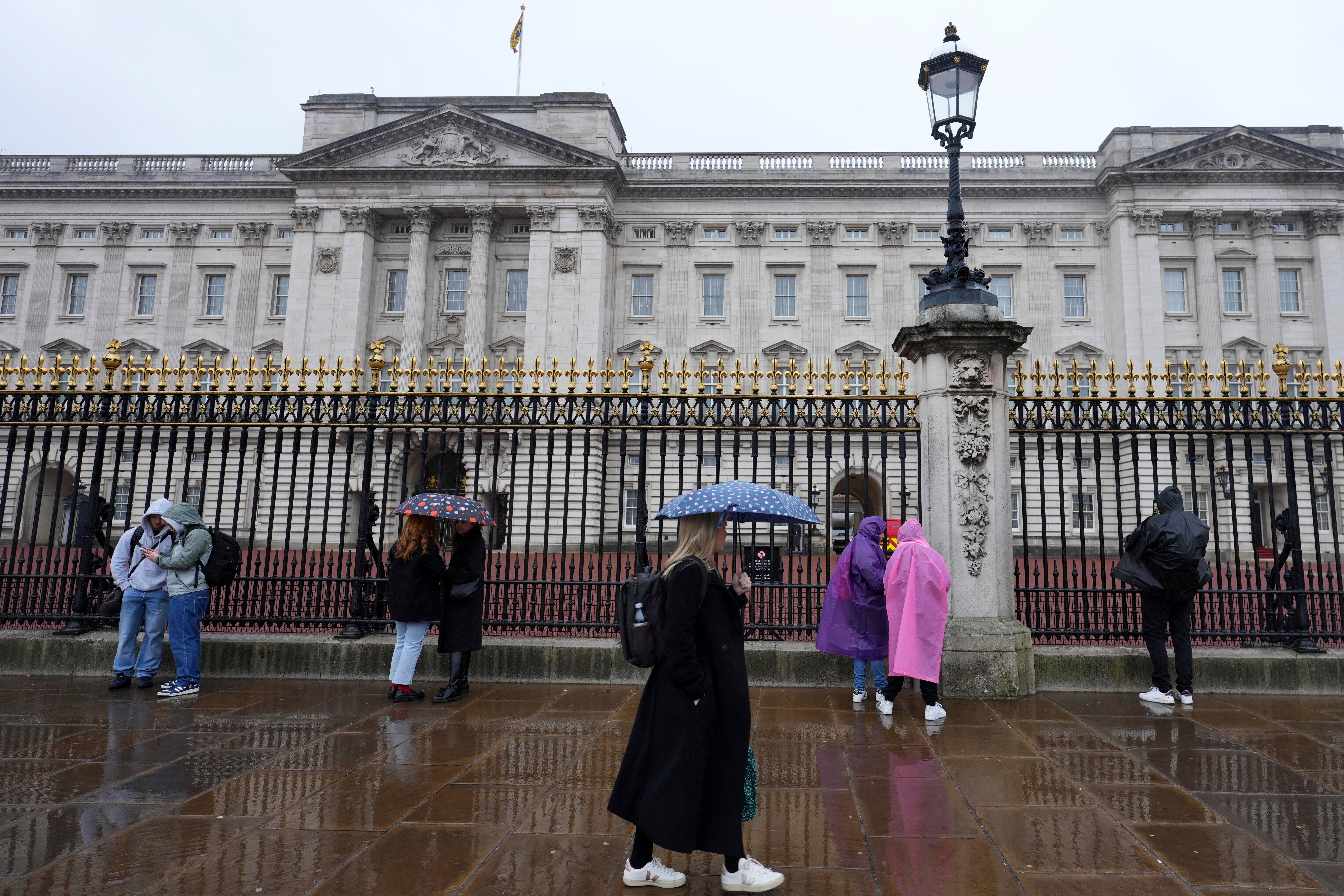 Tourists stand in the rain at Buckingham Palace in London on Friday