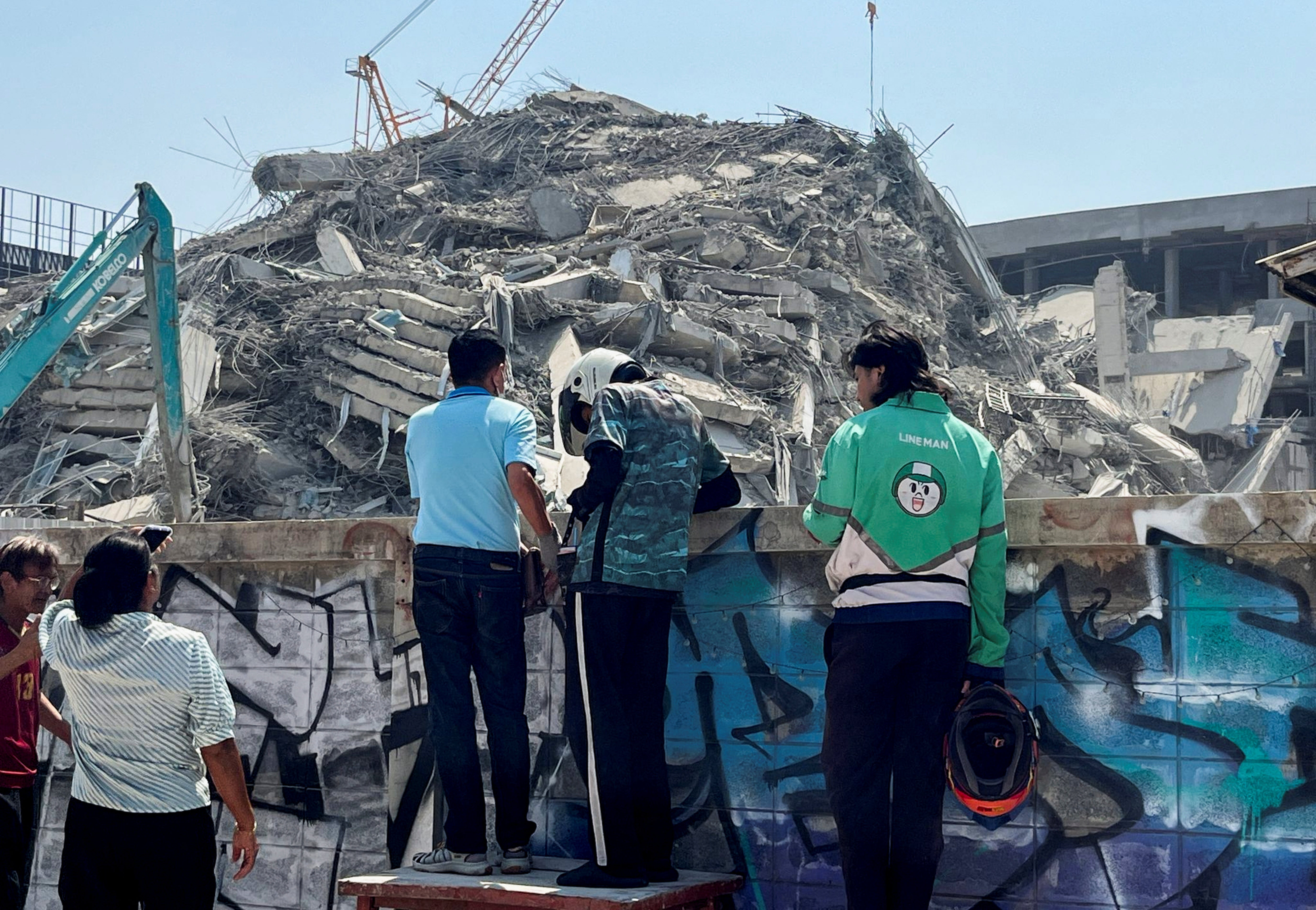 People stand near the site of a collapsed building after a strong earthquake struck central Myanmar on Friday