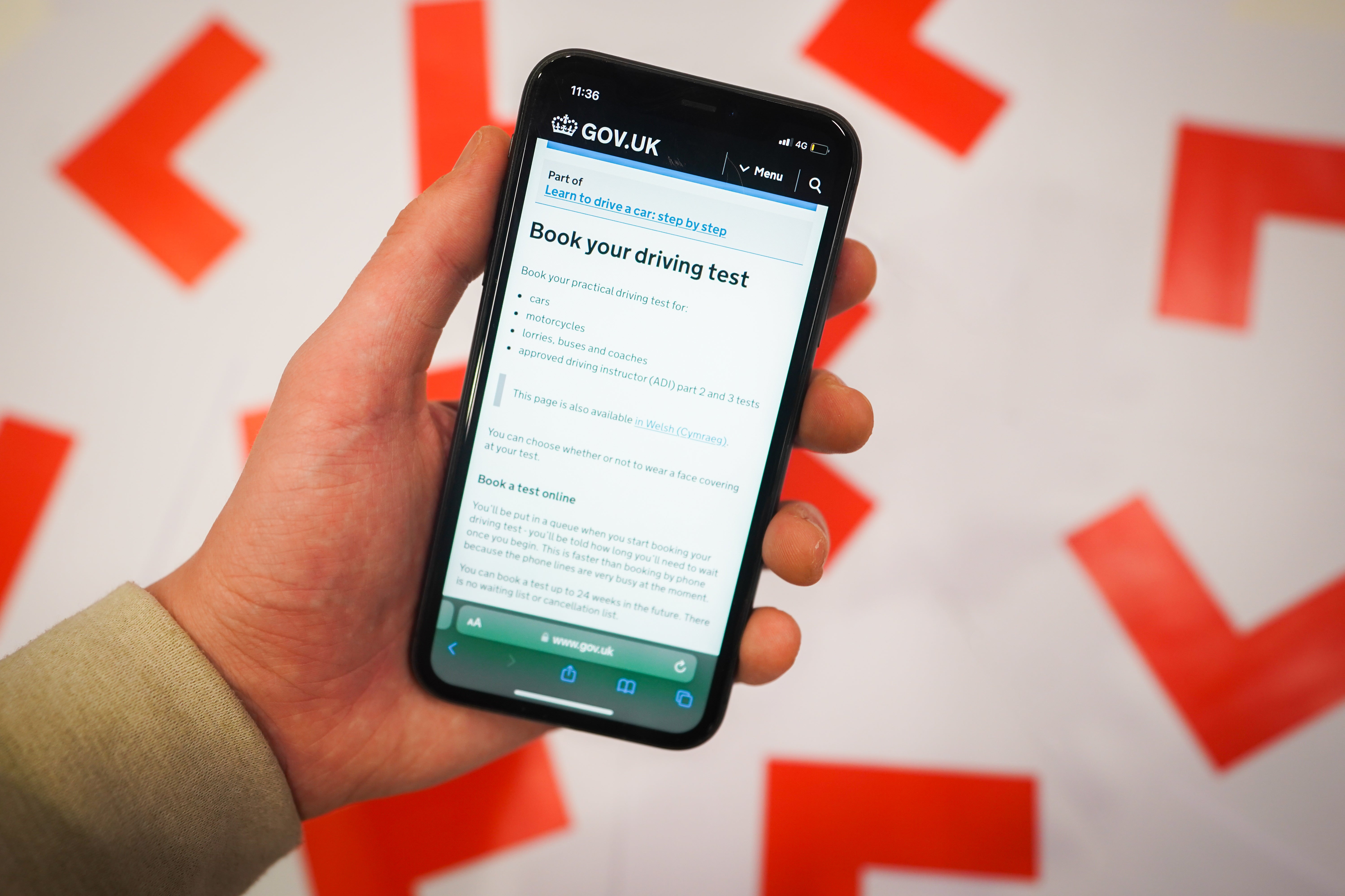 A driving test page on the gov.uk website shown on a phone next to driving L plates