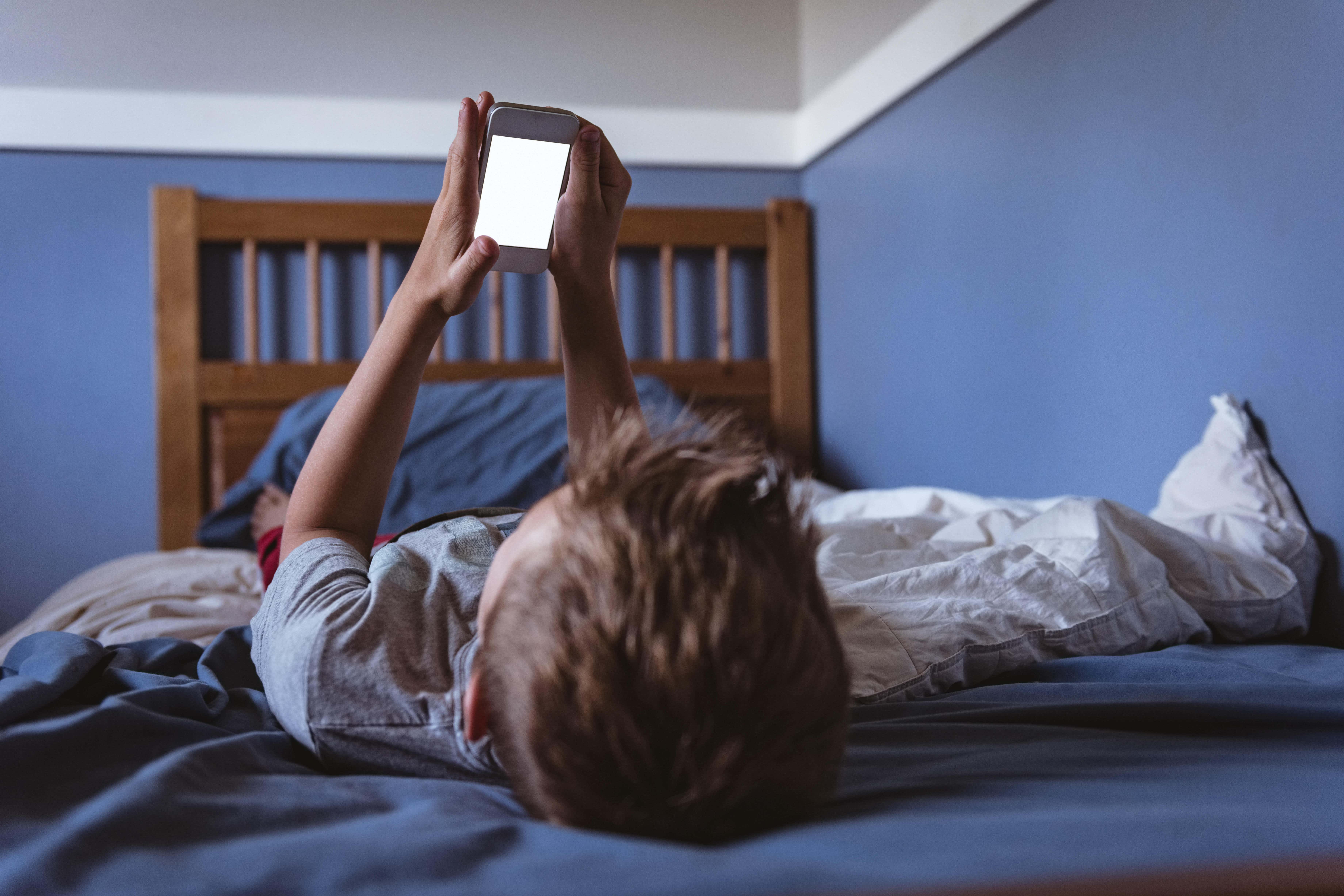A child looks at a phone screen in his bedroom (Alamy/PA)