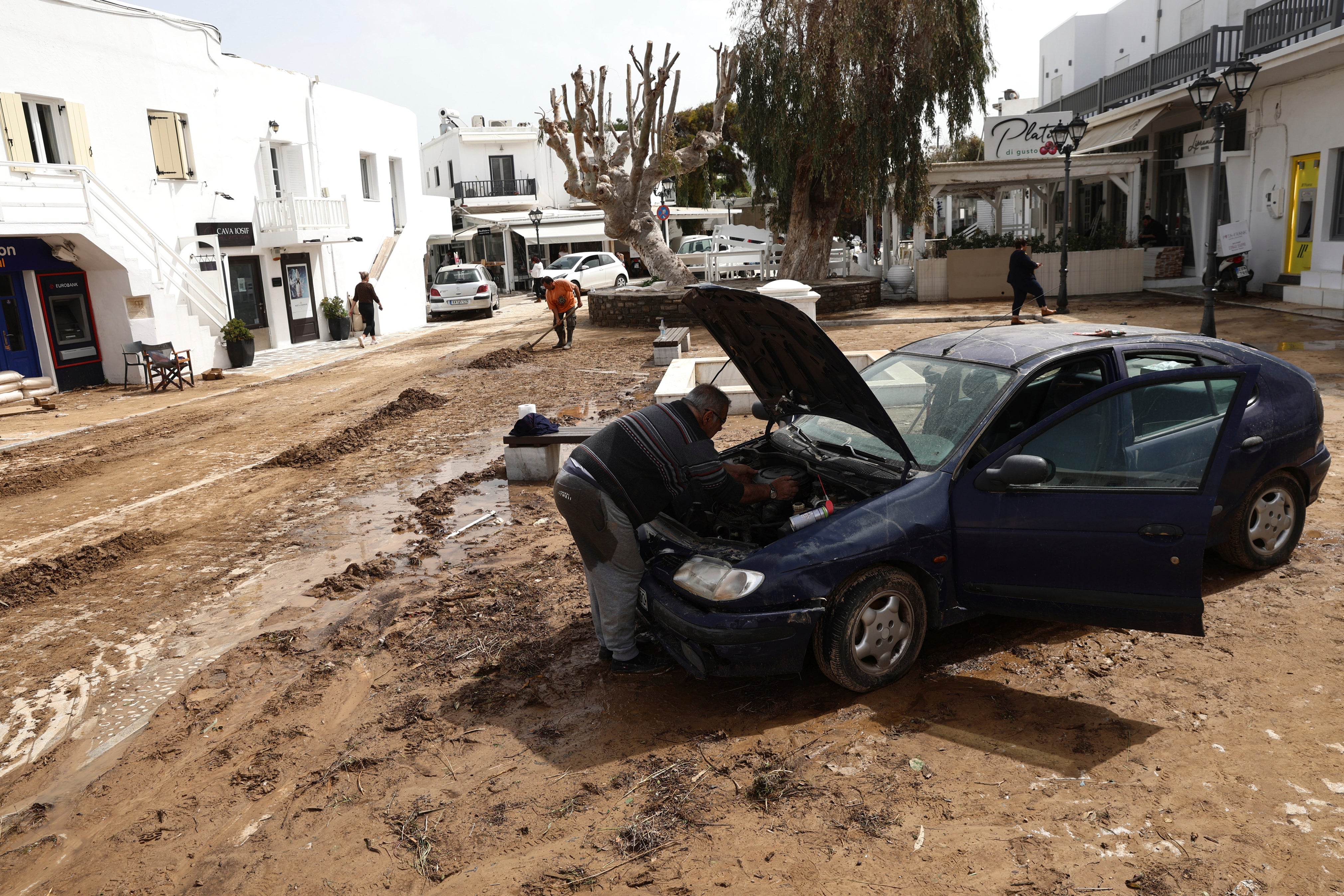 A man tries to fix a car which was inundated in flooding on Paros