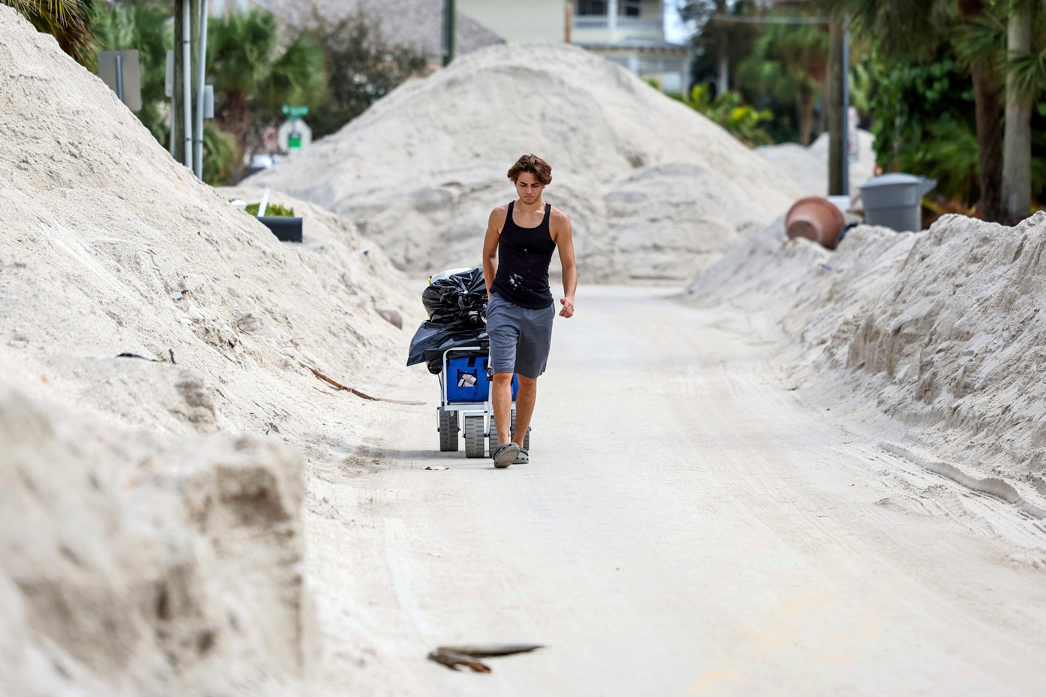 David DeMeza walks out with belongings through sands pushed on to the streets by Hurricane Helene
