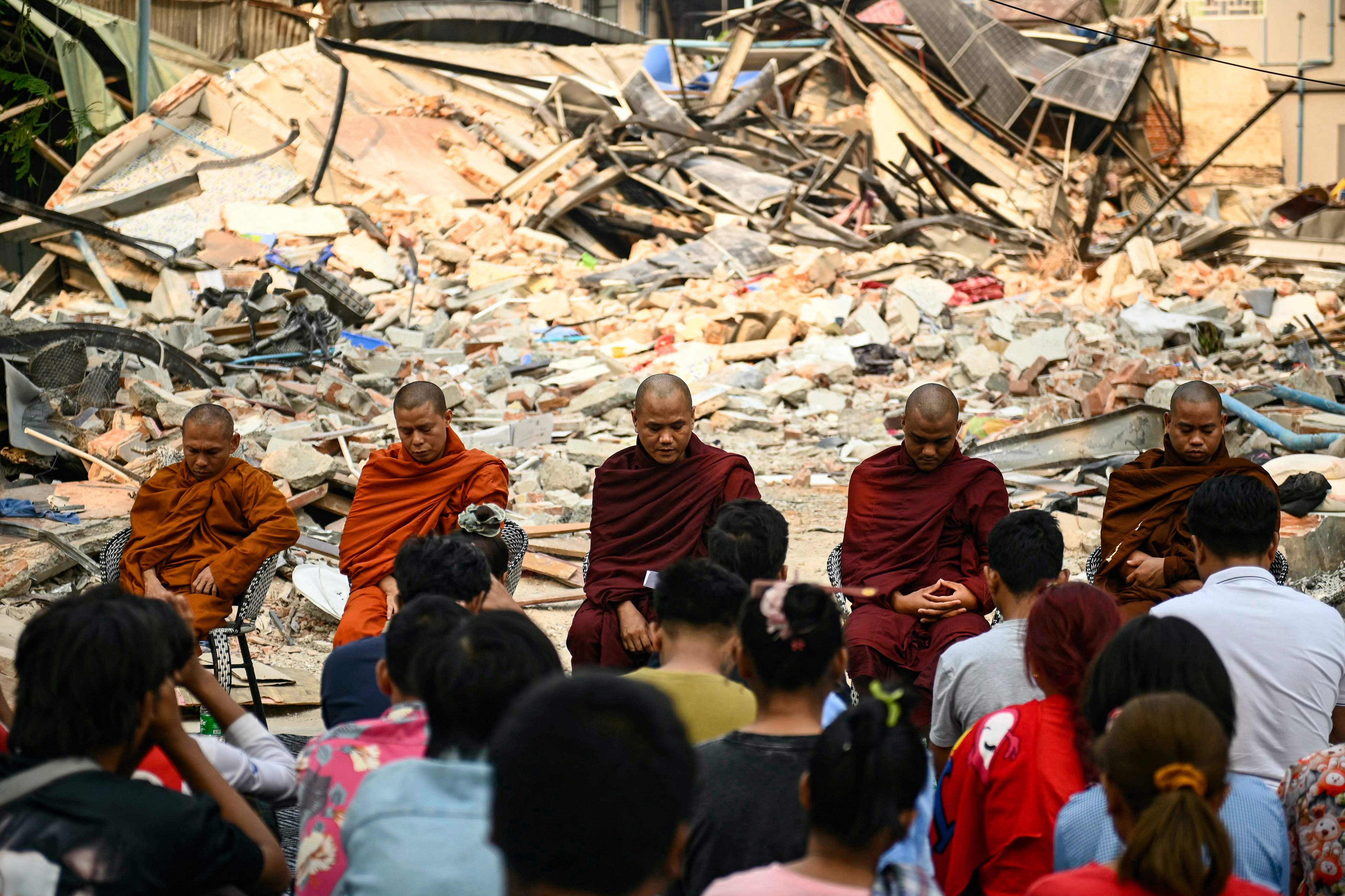 People attend a Buddhist memorial service near the rubble of a collapsed building in Mandalay