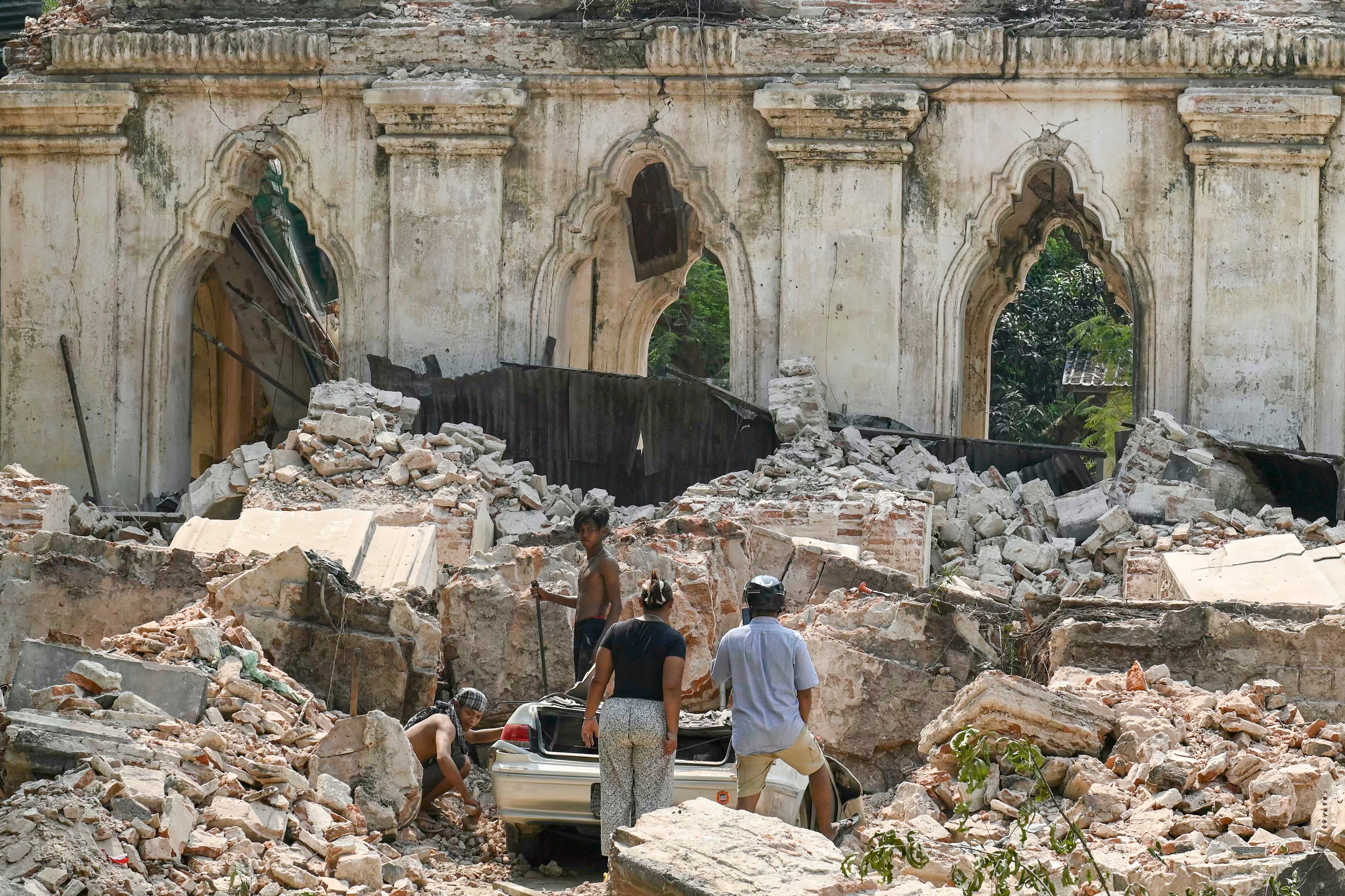 People dig out a car from the rubble of a destroyed building on the outskirts of Mandalay