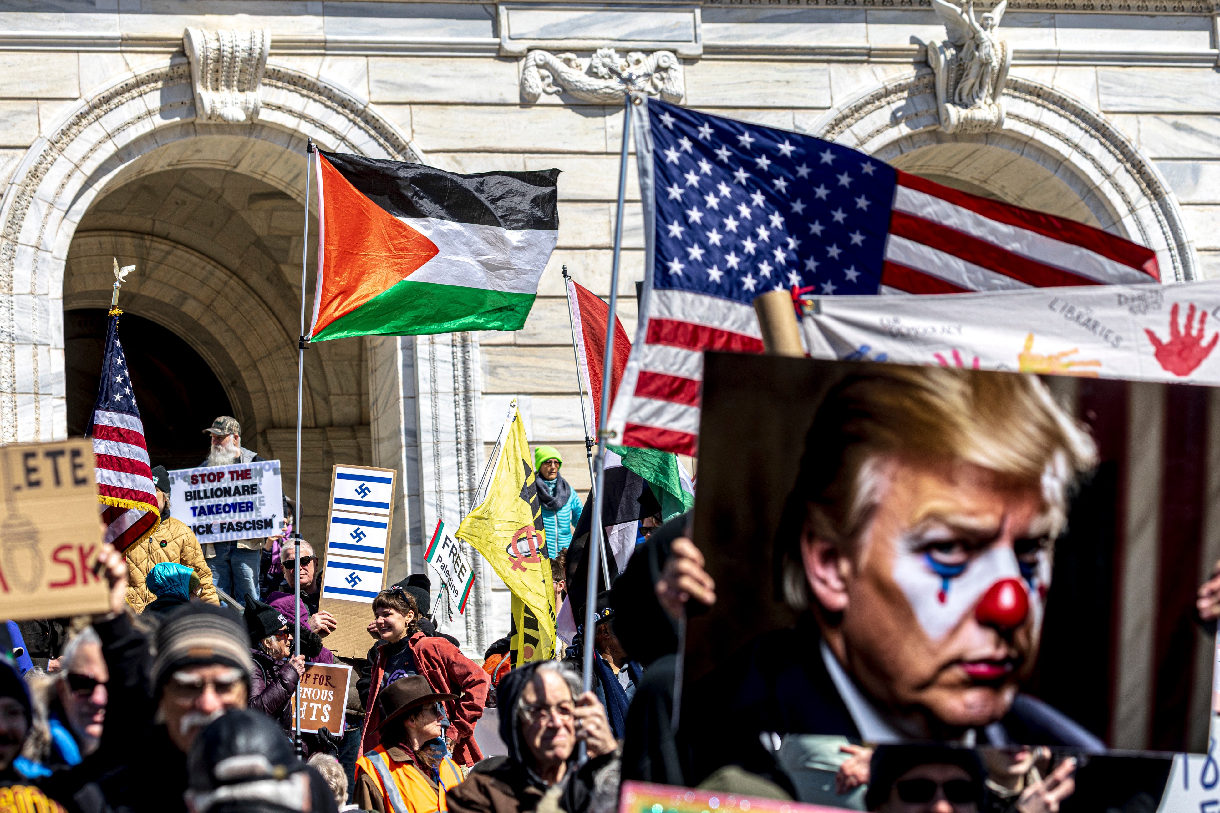 Demonstrators gather outside the Minnesota State Capitol during the nationwide "Hands Off!" protest, with some holding up a sign depicting Trump as a clown