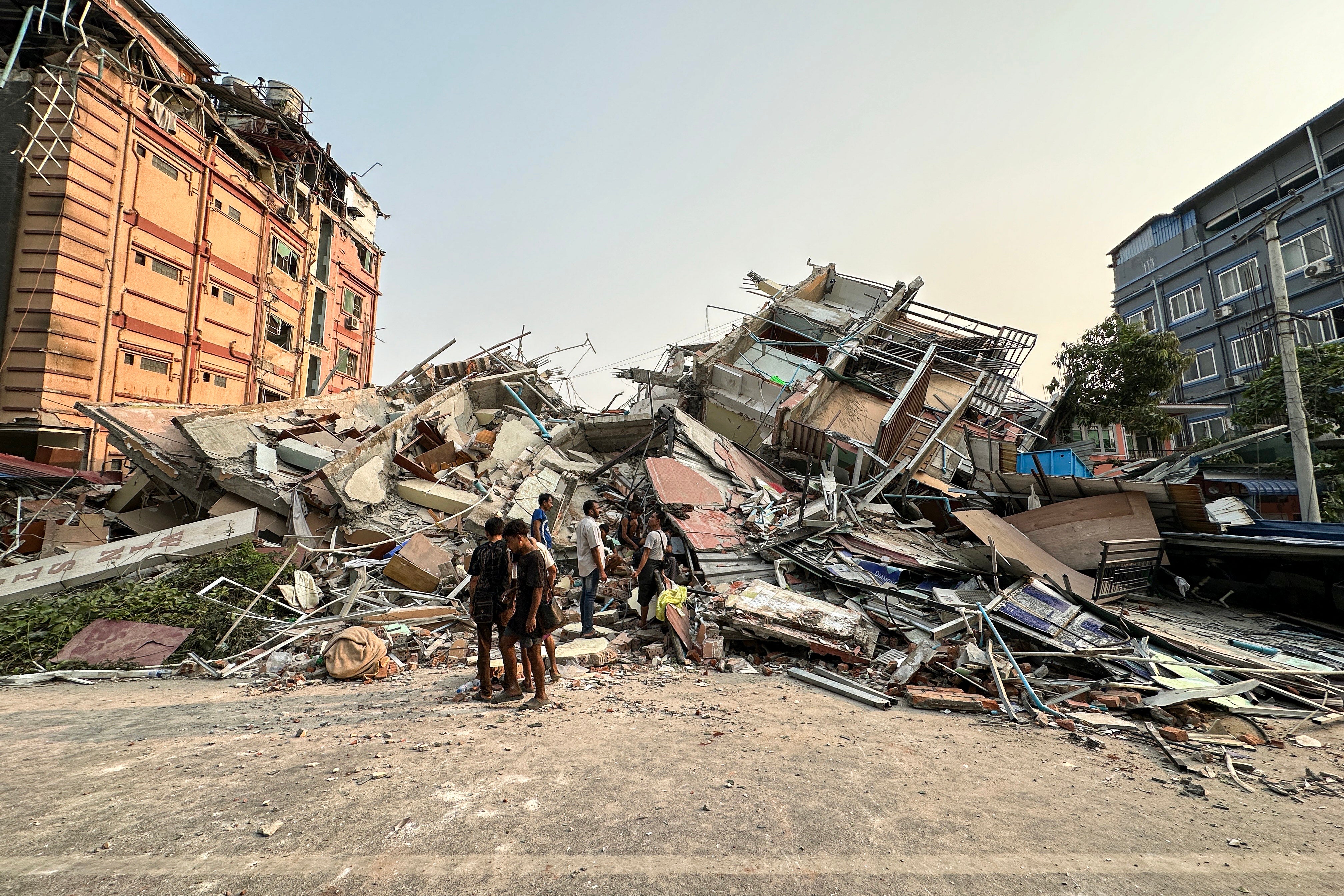 People stand near debris of a collapsed building following an earthquake in Mandalay, Myanmar, on 28 March 2025
