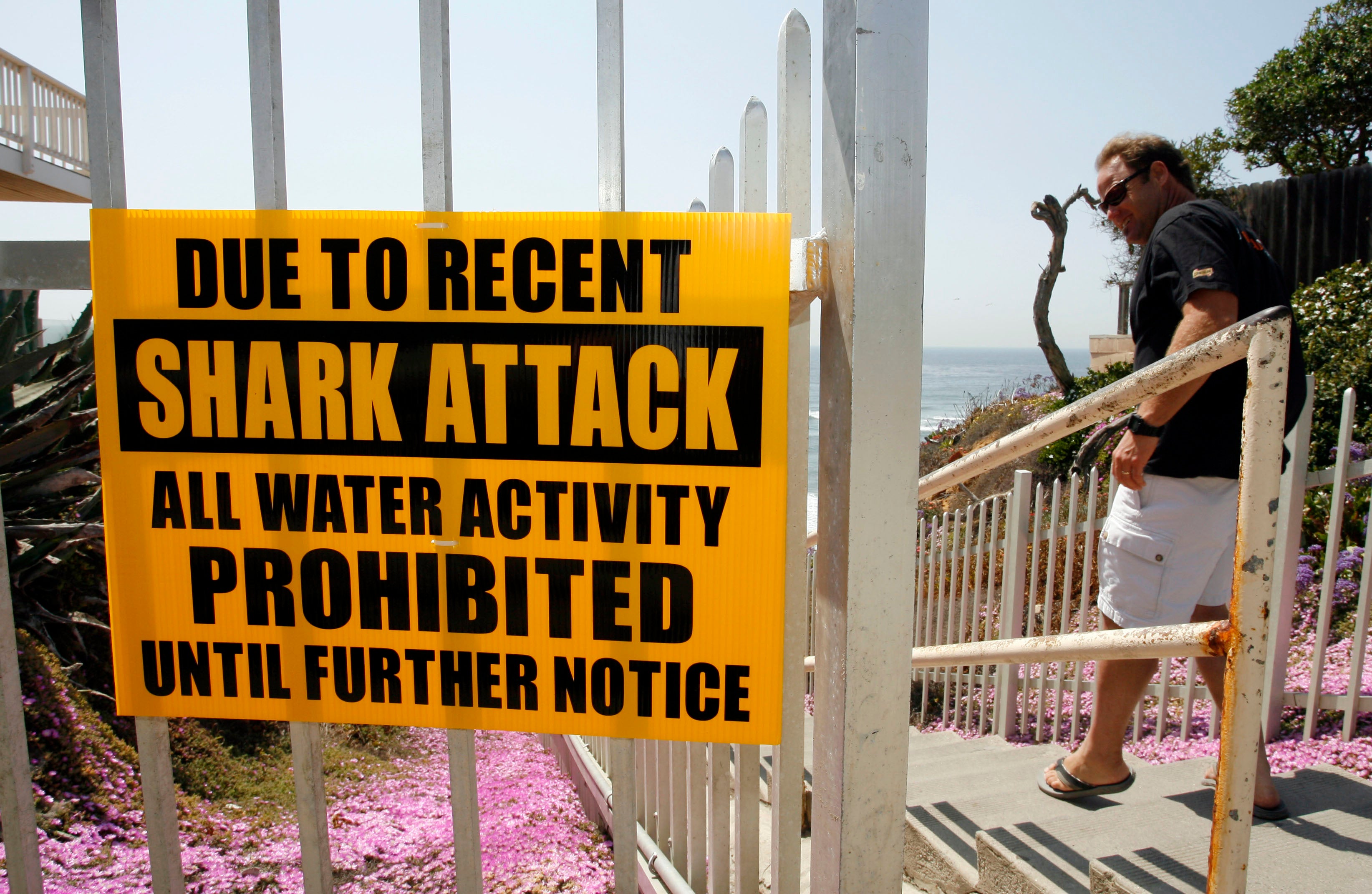 A man walks past a sign prohibiting water activity above Tide Beach after a shark attack in Solana Beach, Calif. Friday, April 25, 2008