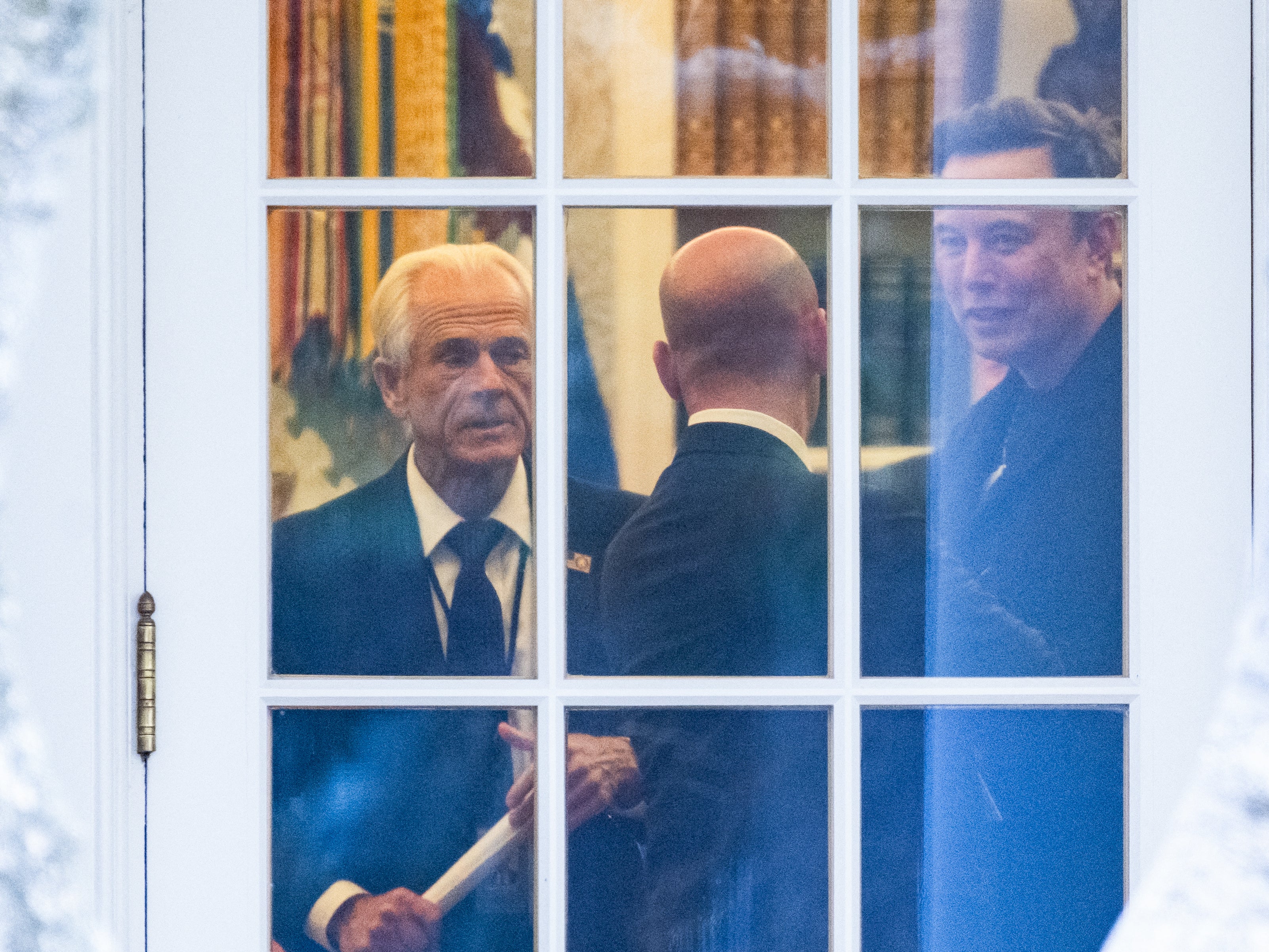 Peter Navarro, left, and Elon Musk are seen through a window in the Oval Office.