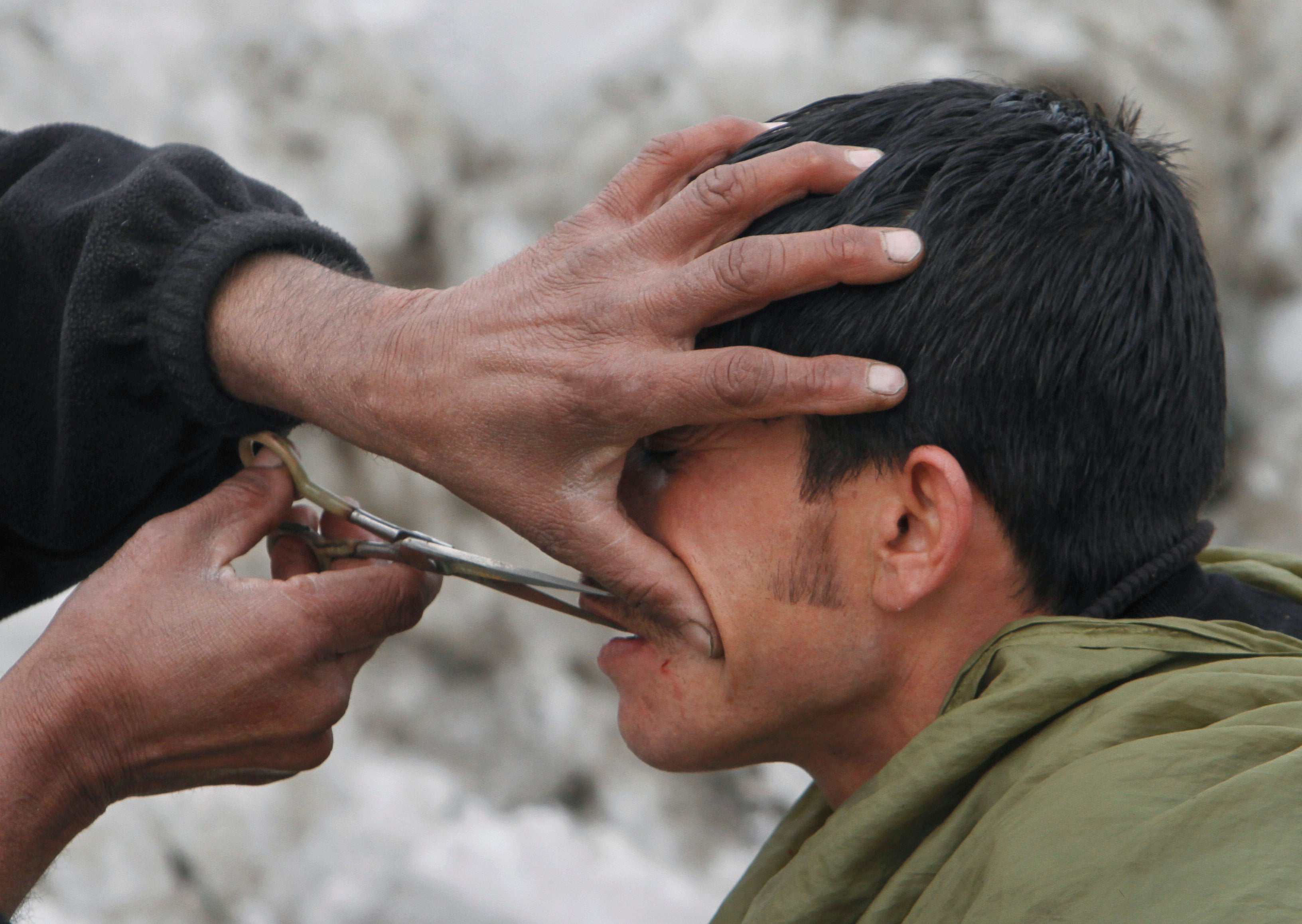 An Afghan street barber trims the mustache of a customer