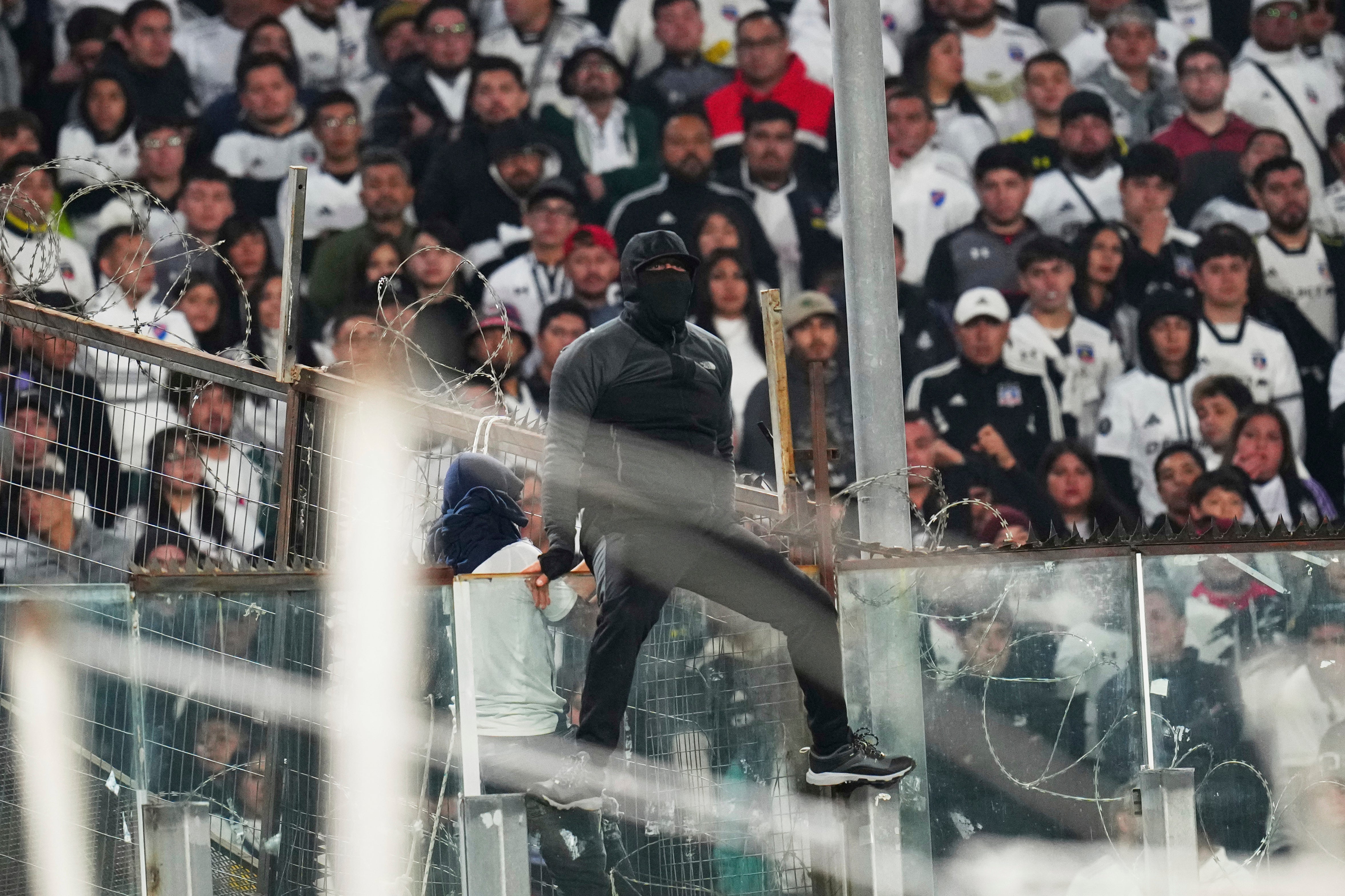 A fan climbs on a glass panel in the stands during a Copa Libertadores Group E soccer match between Chile's Colo Colo and Brazil's Fortaleza at Monumental Stadium in Santiago, Chile, Thursday, April 10, 2025