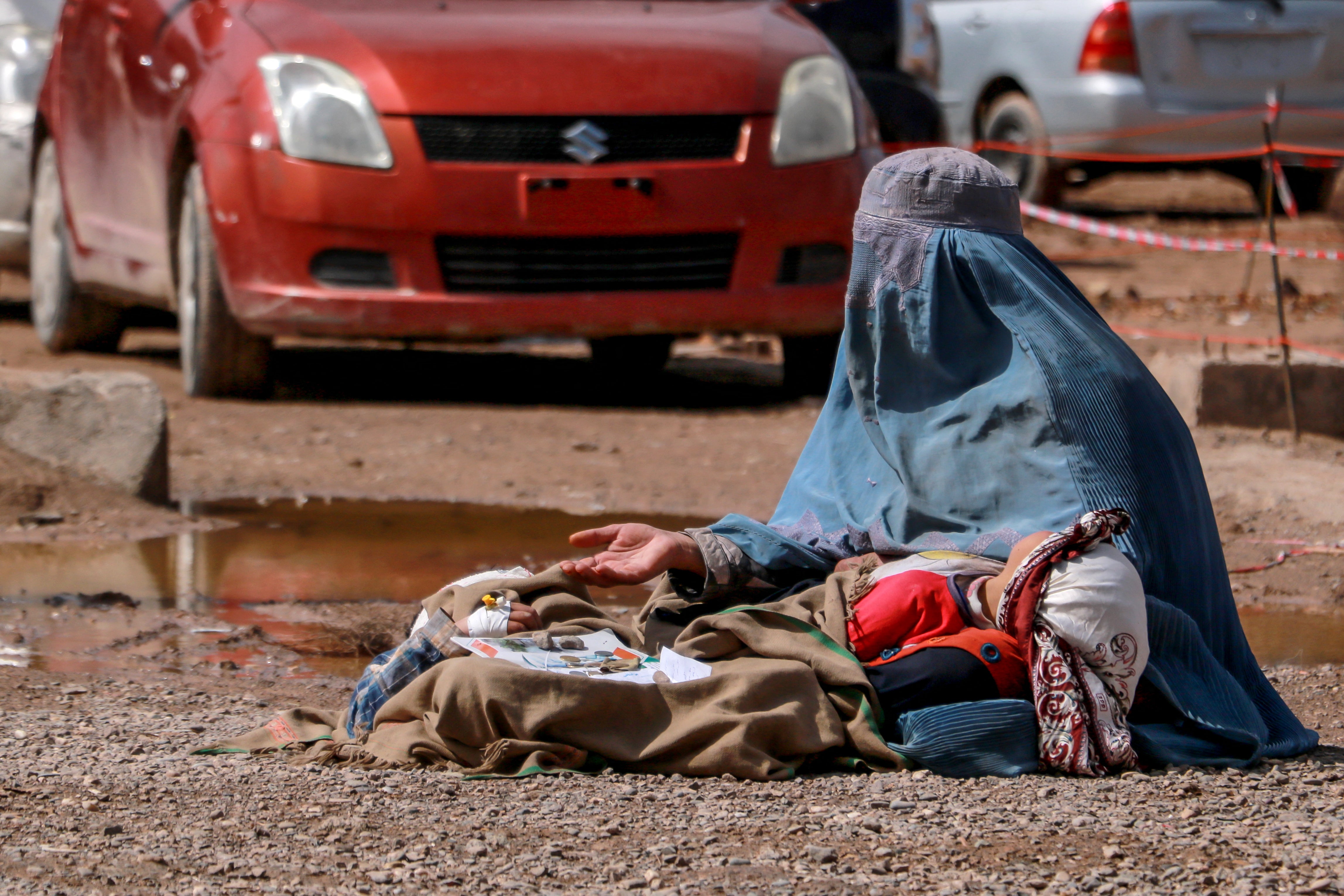 An Afghan woman holds a child as she seeks alms by a road in Herat