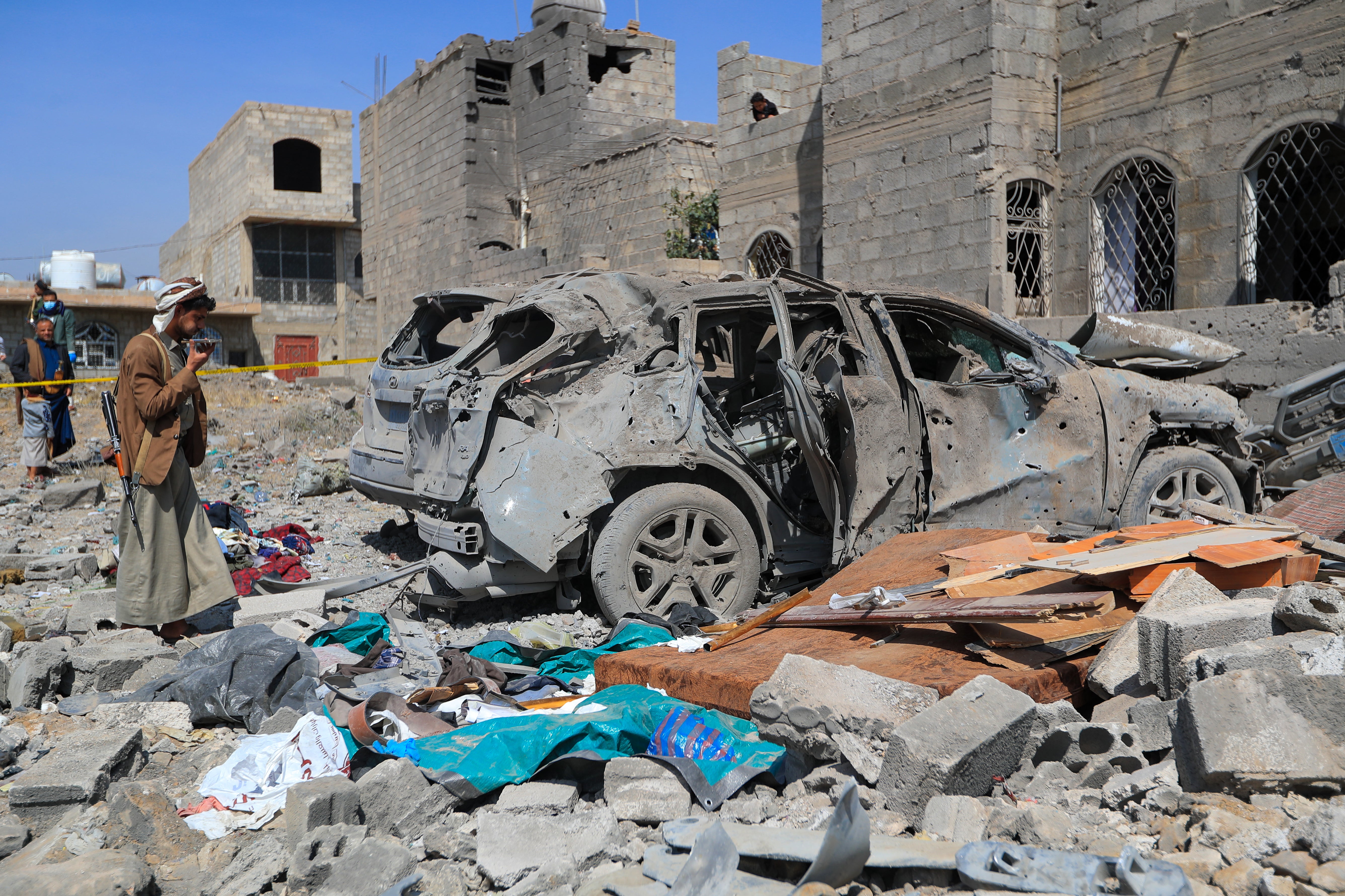 File. An armed man speaks on his mobile phone as he checks the wreckage of a car at the site of a reported US airstrike in Sanaa on 7 April 2025