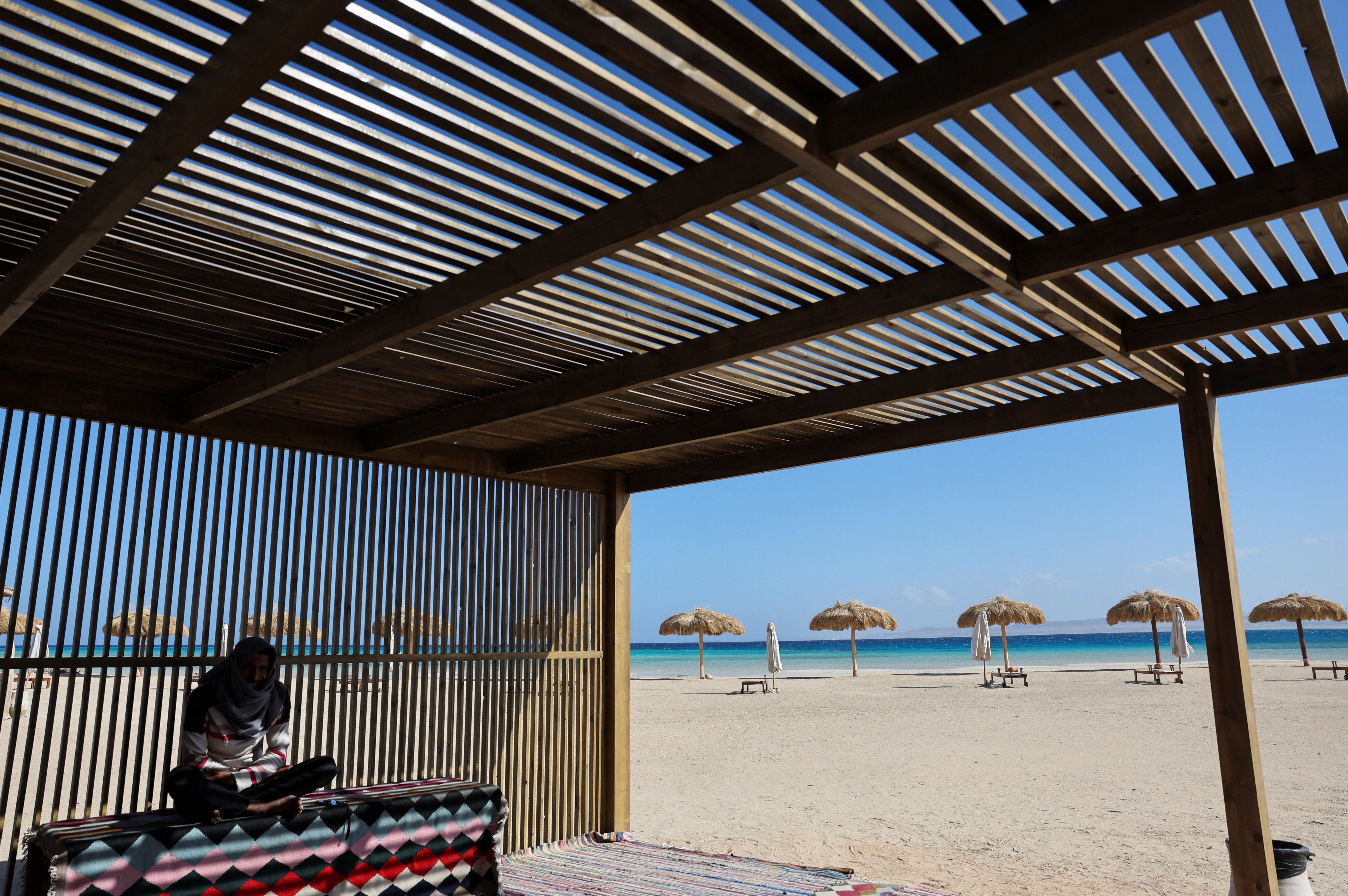 A man sits under a wooden structure at Ras Hankorab beach, home to one of the country's last untouched marine ecosystems, with crystal clear waters and white sands, at southern Egypt's Red Sea coast in Marsa Alam, Egypt