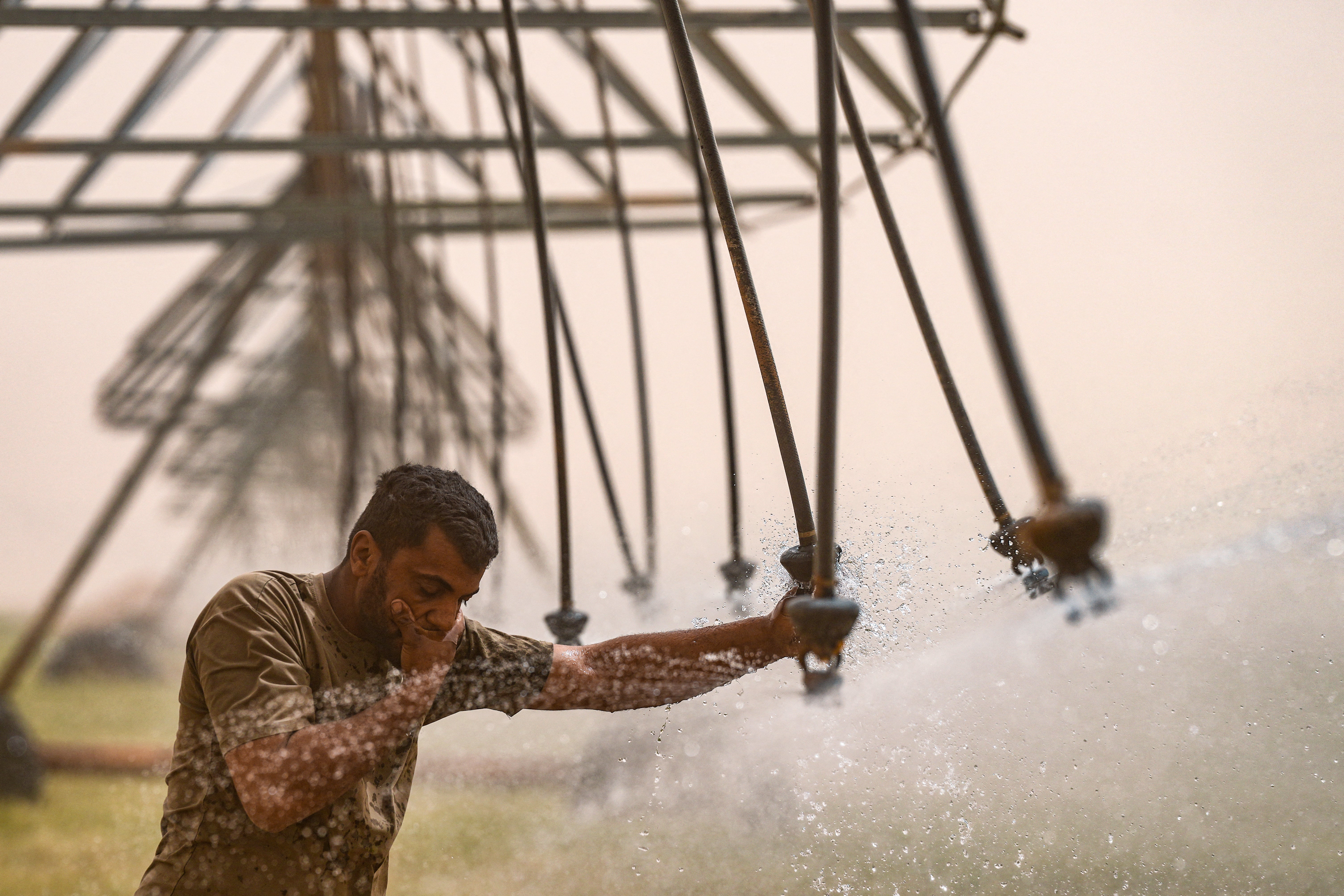 An Iraqi worker wipes his face with water from a modern irrigation sprinkler system in a wheat field in the desert of Najaf as a heavy sandstorm hit the area in central Iraq on 10 April 2025