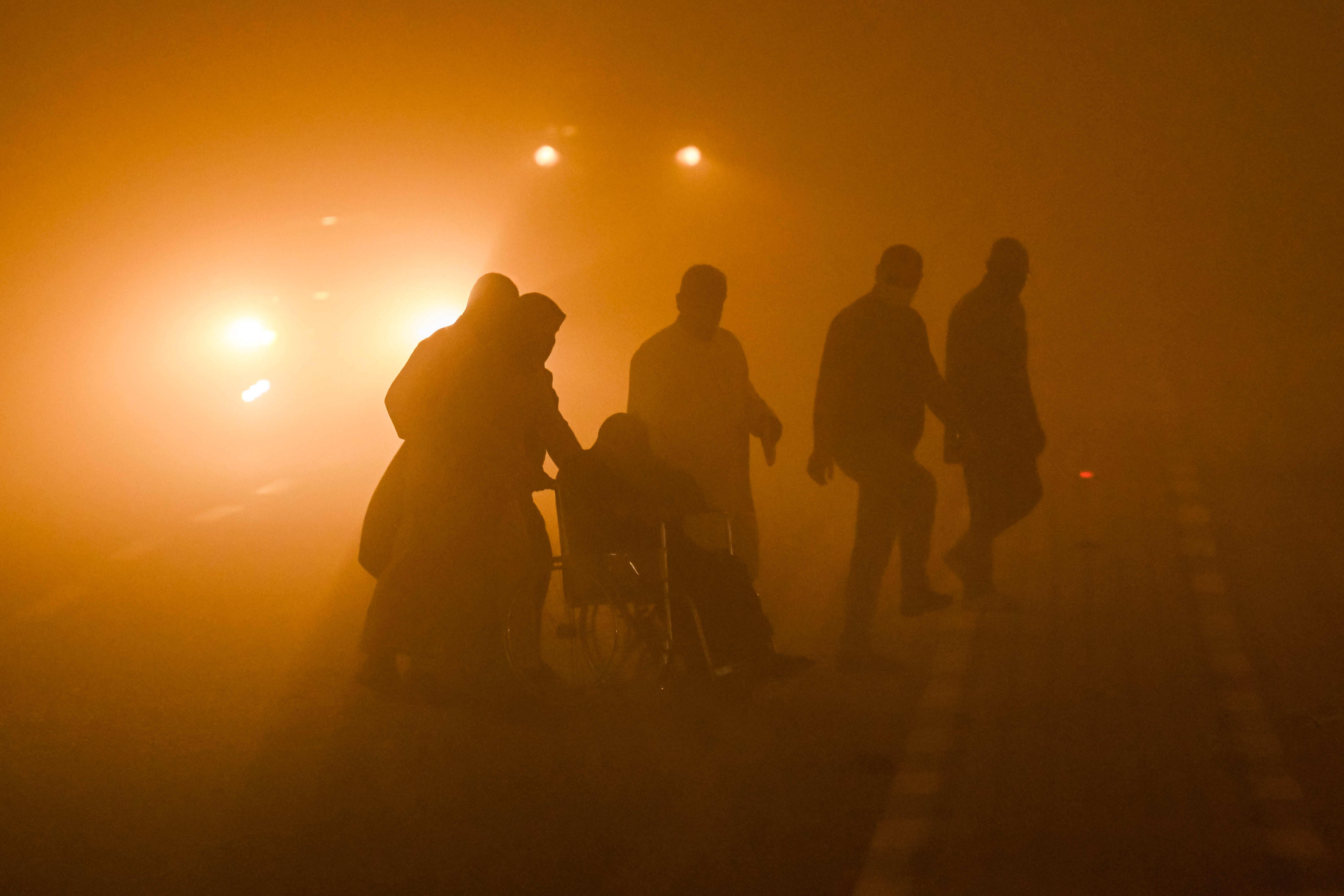A wheelchair-bound person is assisted by others to cross to a traffic island in the middle of a road in low visibility conditions amidst a massive dust storm in Iraq's southern city of Basra on 14 April 2025