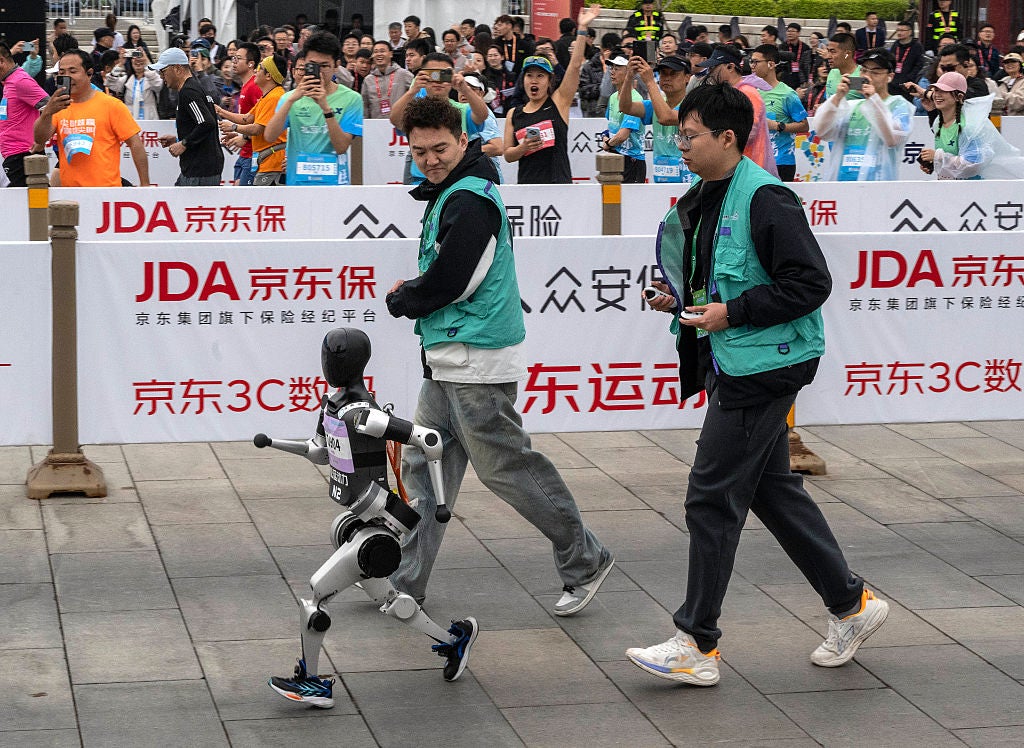 A humanoid robot with technicians competes in the Beijing E-Town Humanoid Robot Half Marathon on Saturday