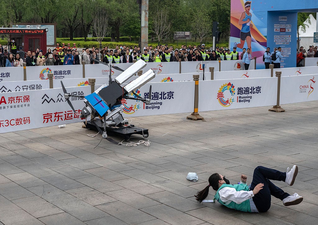 A support technician falls as a humanoid robot crashes while running
