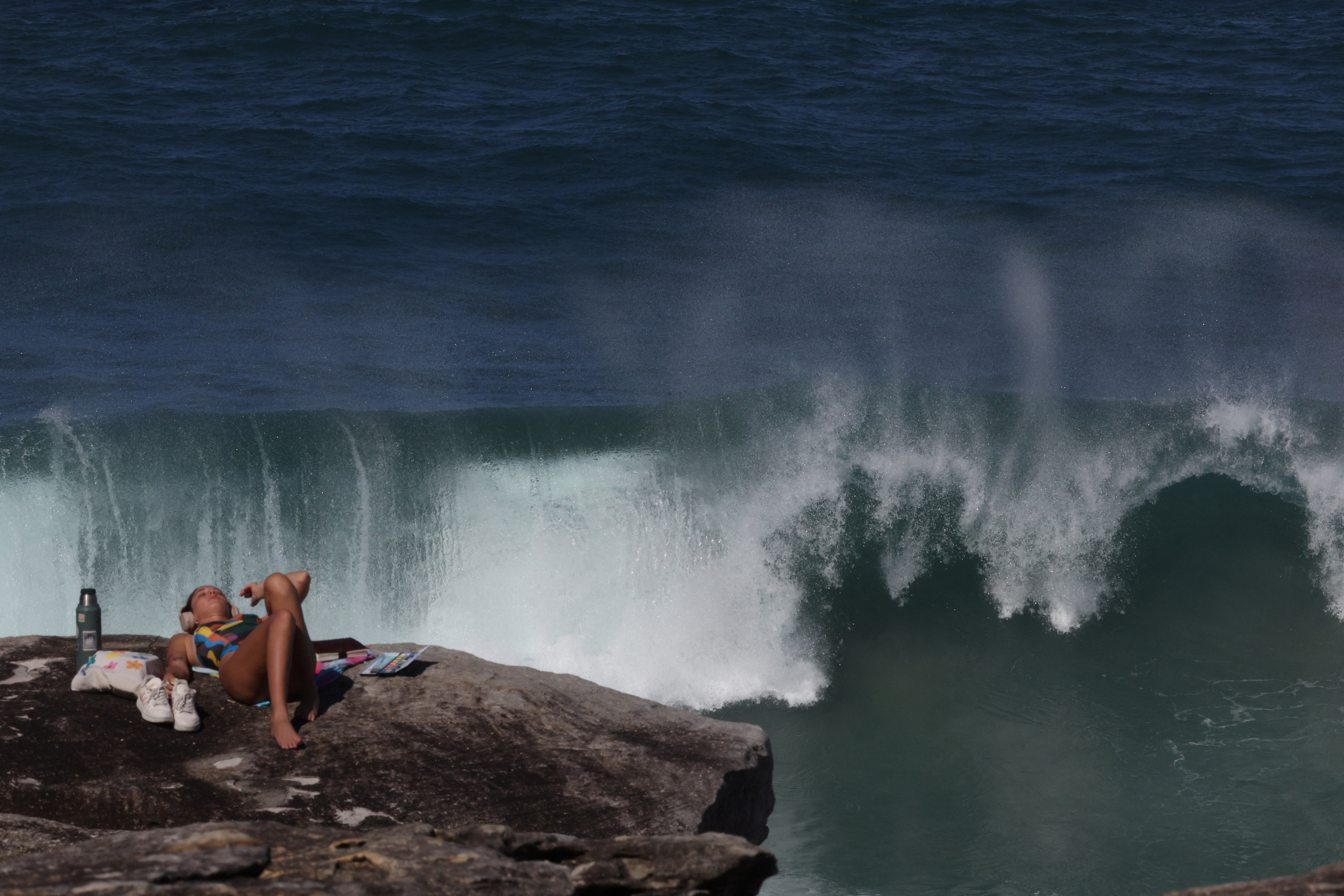A tourist enjoys a sunny morning at Tamarama Beach as large waves crash against a rock in Sydney
