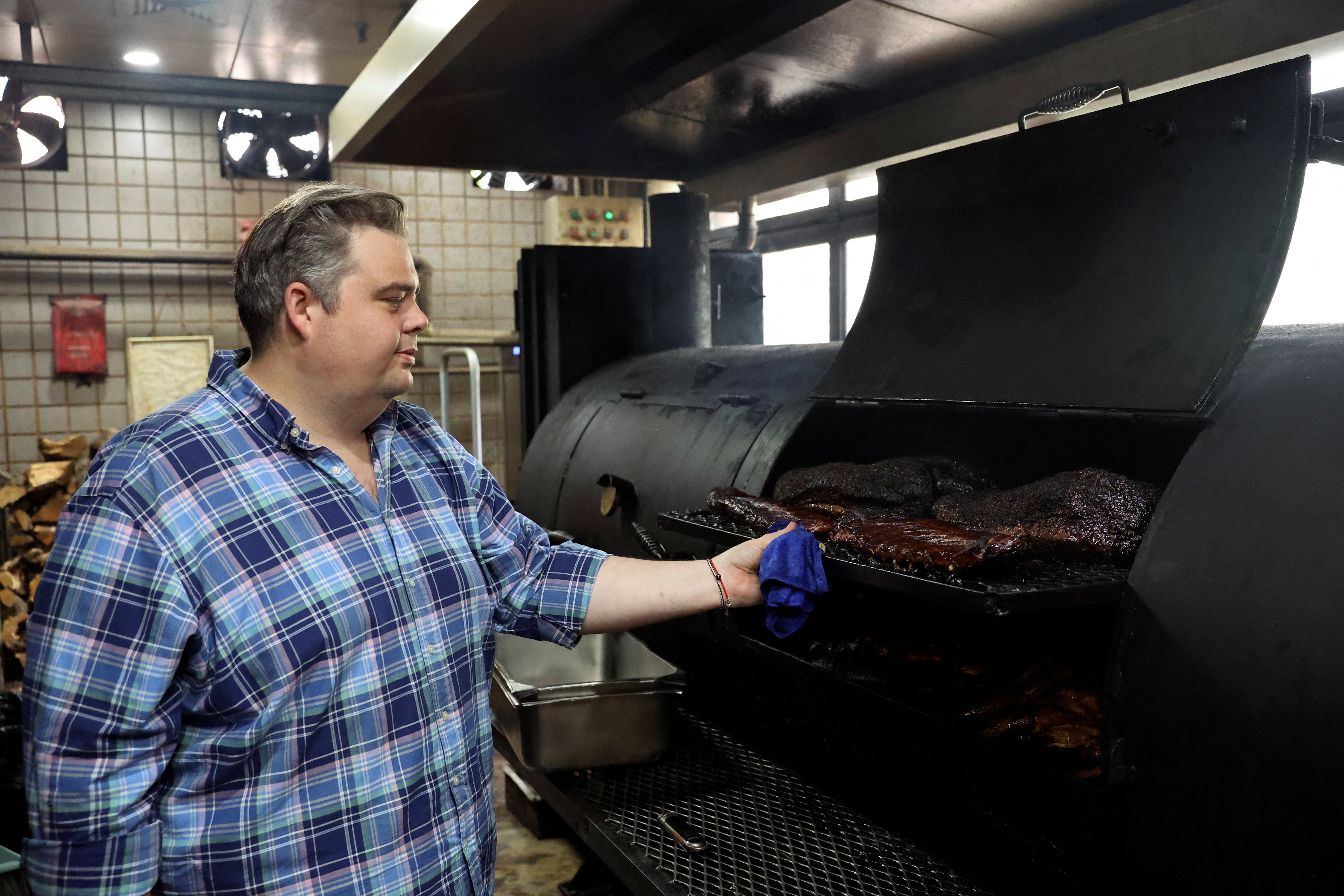 Charles de Pellette, Operations Director of the restaurant, poses for a picture next to U.S. beef and pork in a smokehouse, at Home Plate BBQ, an American-style restaurant, in Beijing, China April 17, 2025. REUTERS/Tiffany Le