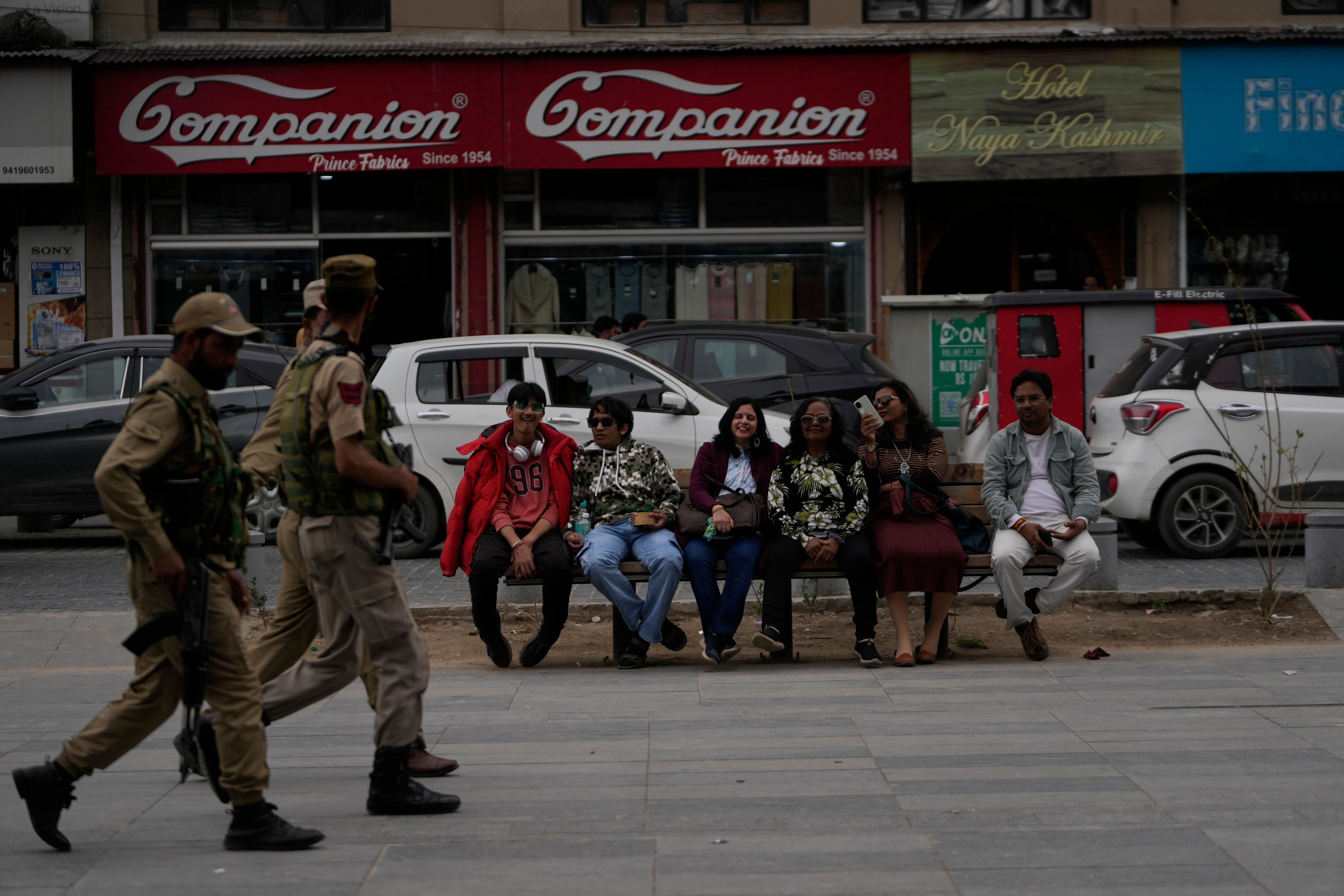 Indian tourists rests on a bench as policemen guard near a clock tower at city centre in Srinagar, Indian controlled Kashmir,Tuesday, 22 April 2025
