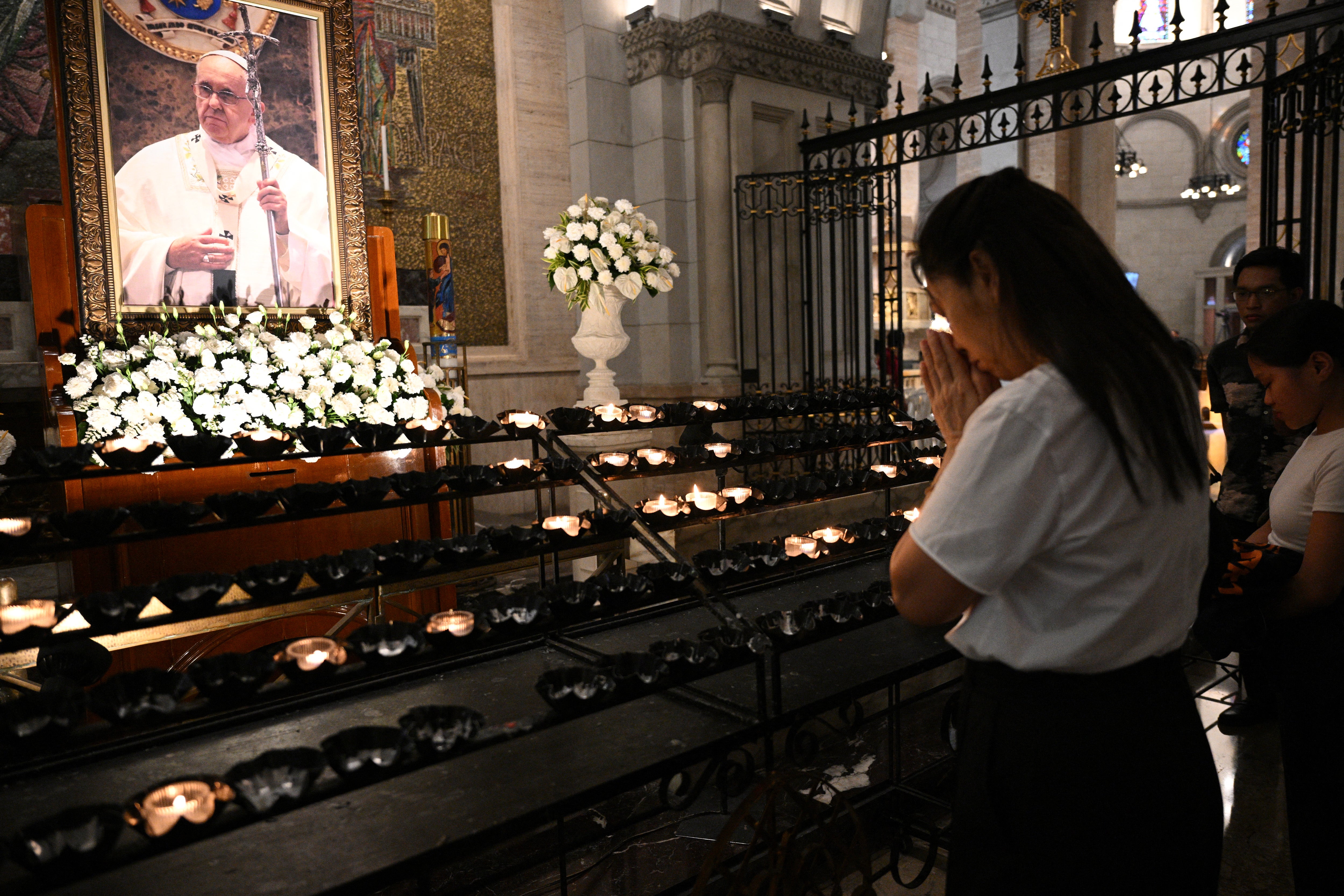 A woman offers prayers in front of a portrait of Pope Francis prior to a requiem mass at the Manila Cathedral in Manila