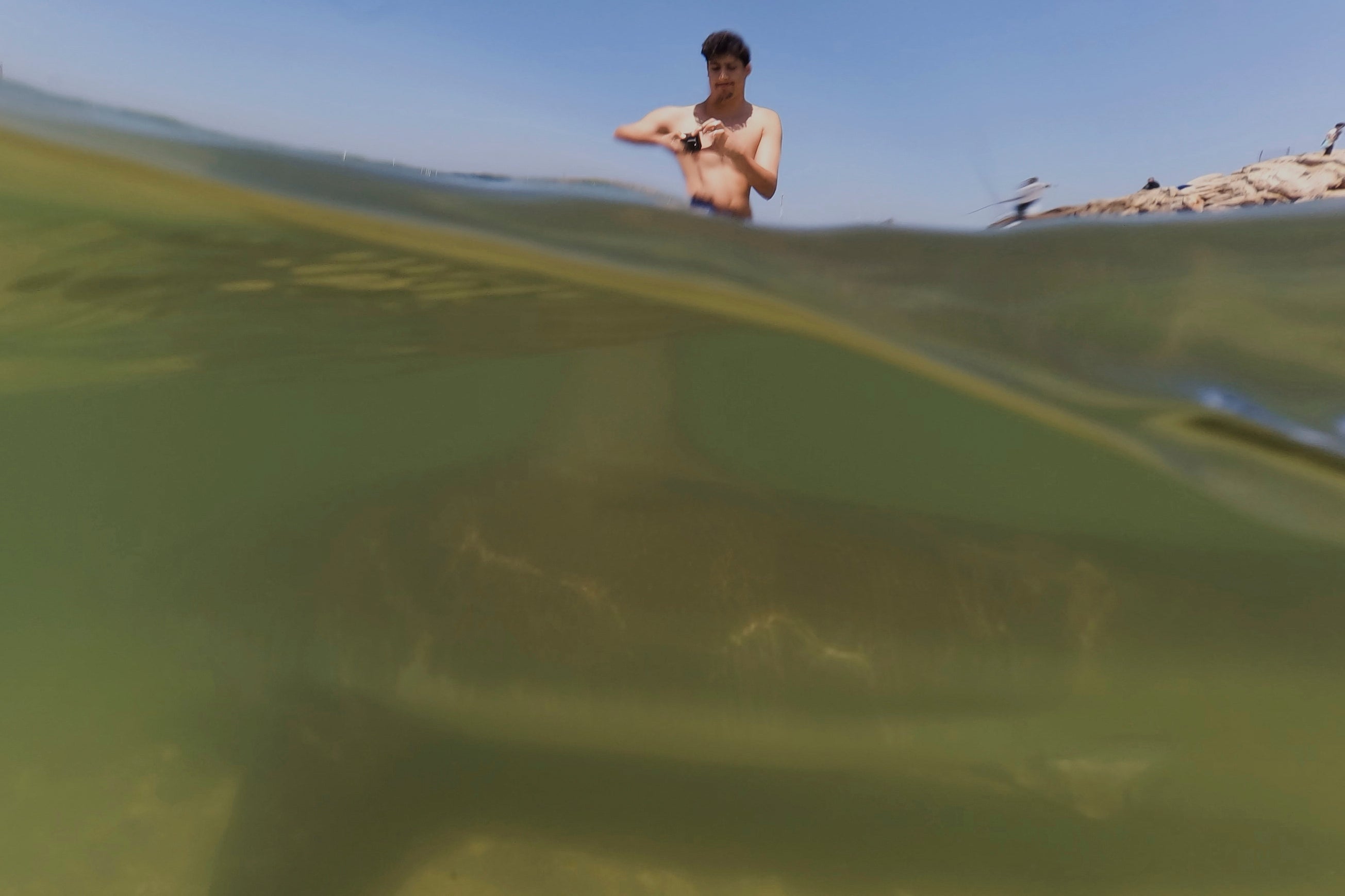 A man records video of a shark swimming in Mediterranean Sea in Hadera, Israel, Saturday, April 19, 2025. (AP Photo/Ariel Schalit)