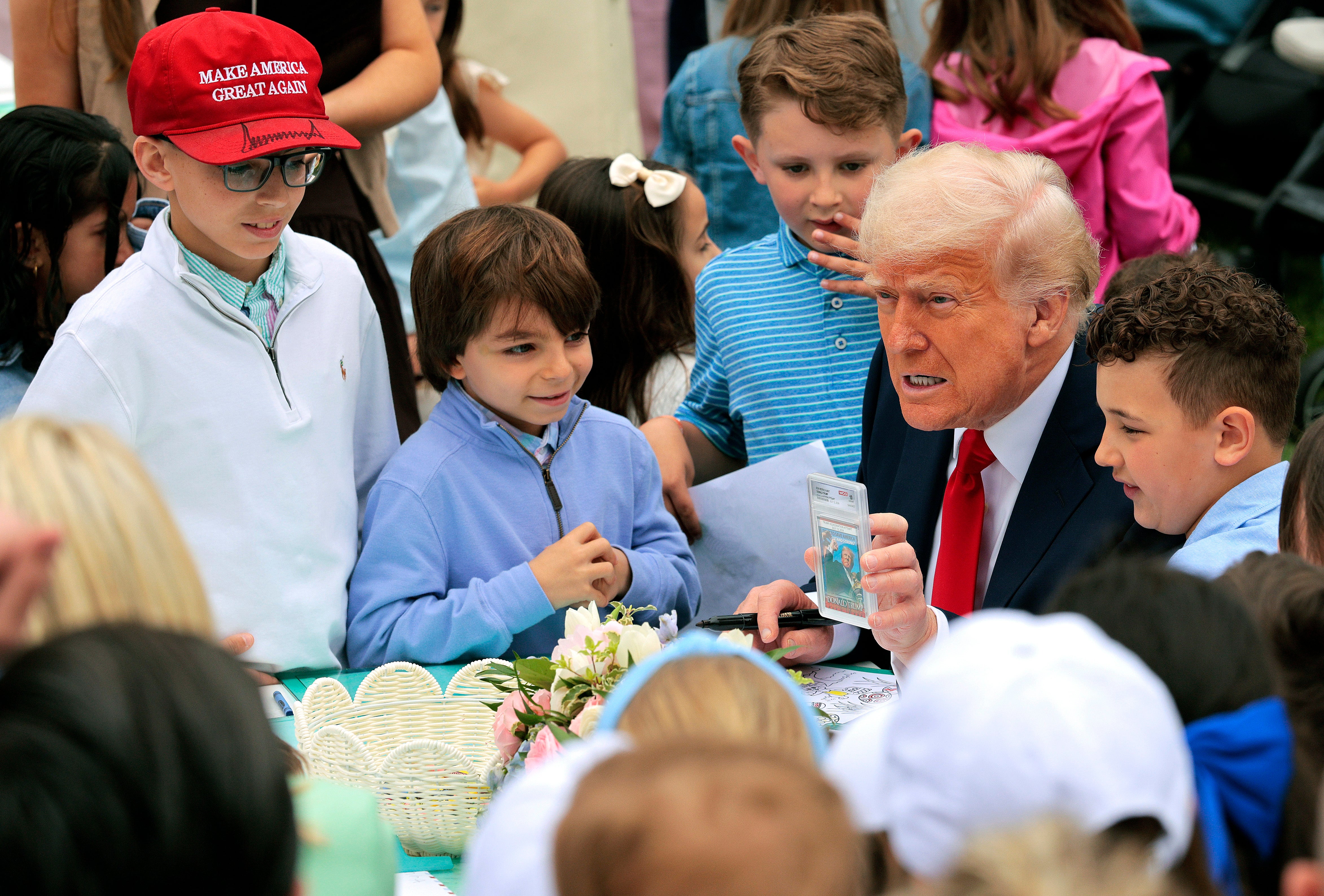 Trump proudly show some school children his trading cards, including one that shows him directly after he survived an assassination attempt