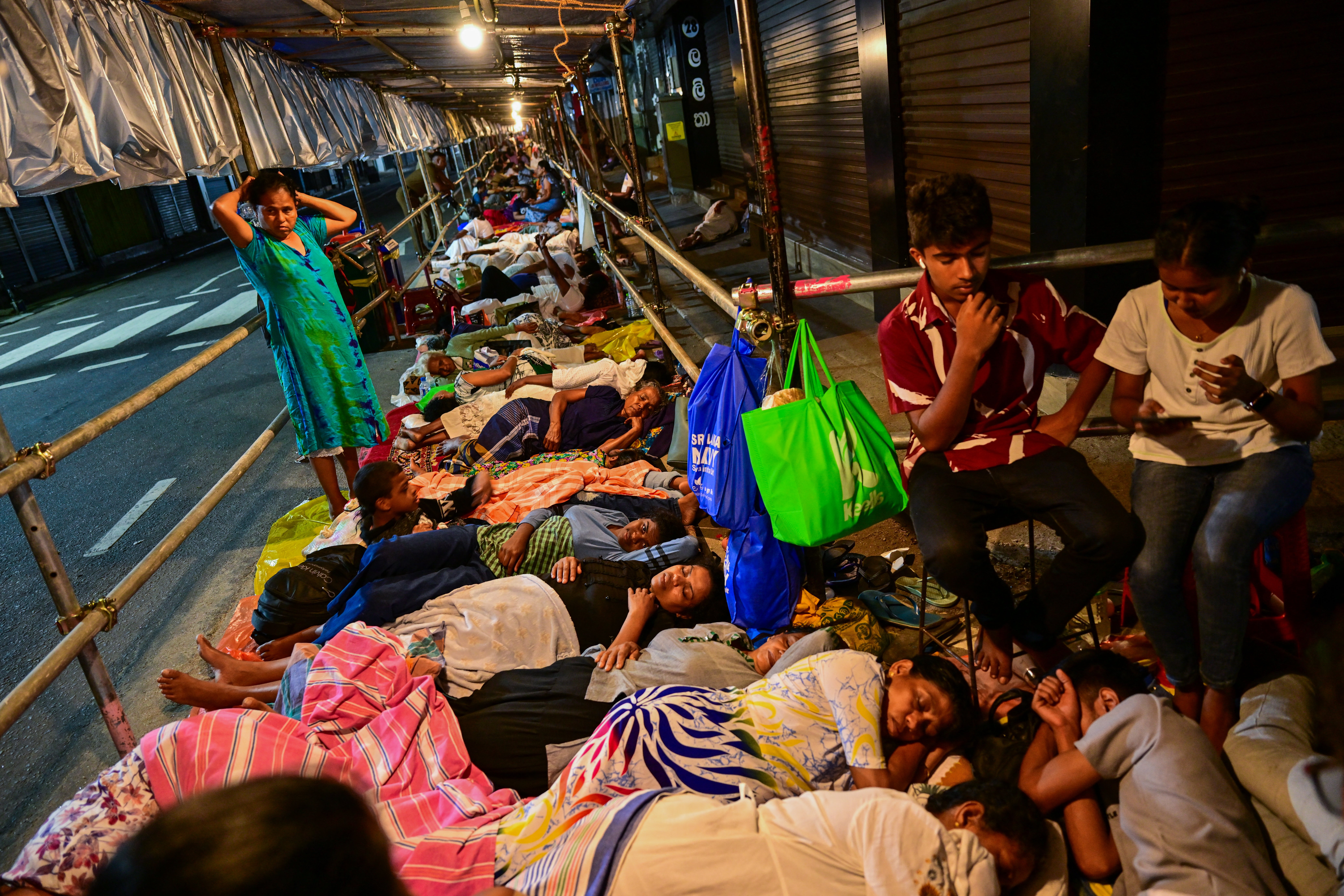 Faithful rest on a pavement under a scaffold to queue overnight at Sri Lanka's holiest Buddhist temple, the Temple of the Tooth, in Kandy on 18 April 2025