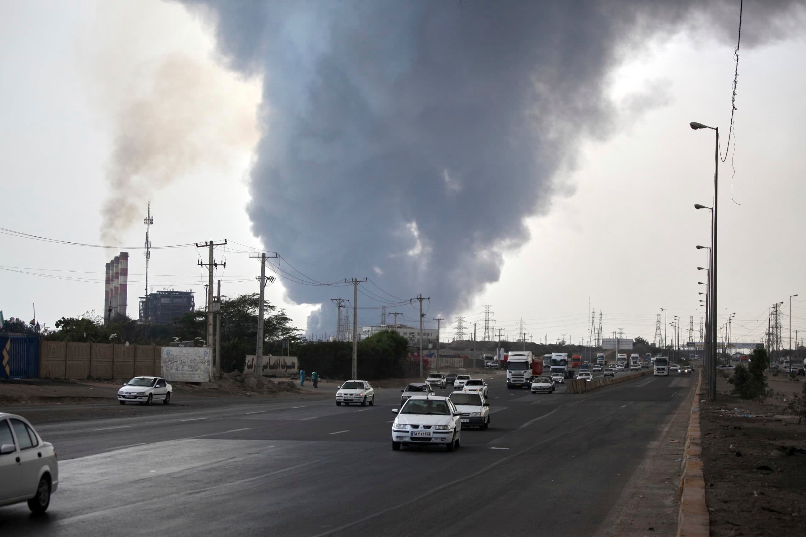 Black smoke rises in the sky as vehicles drive on the road after a massive explosion near the southern port city of Bandar Abbas, Iran